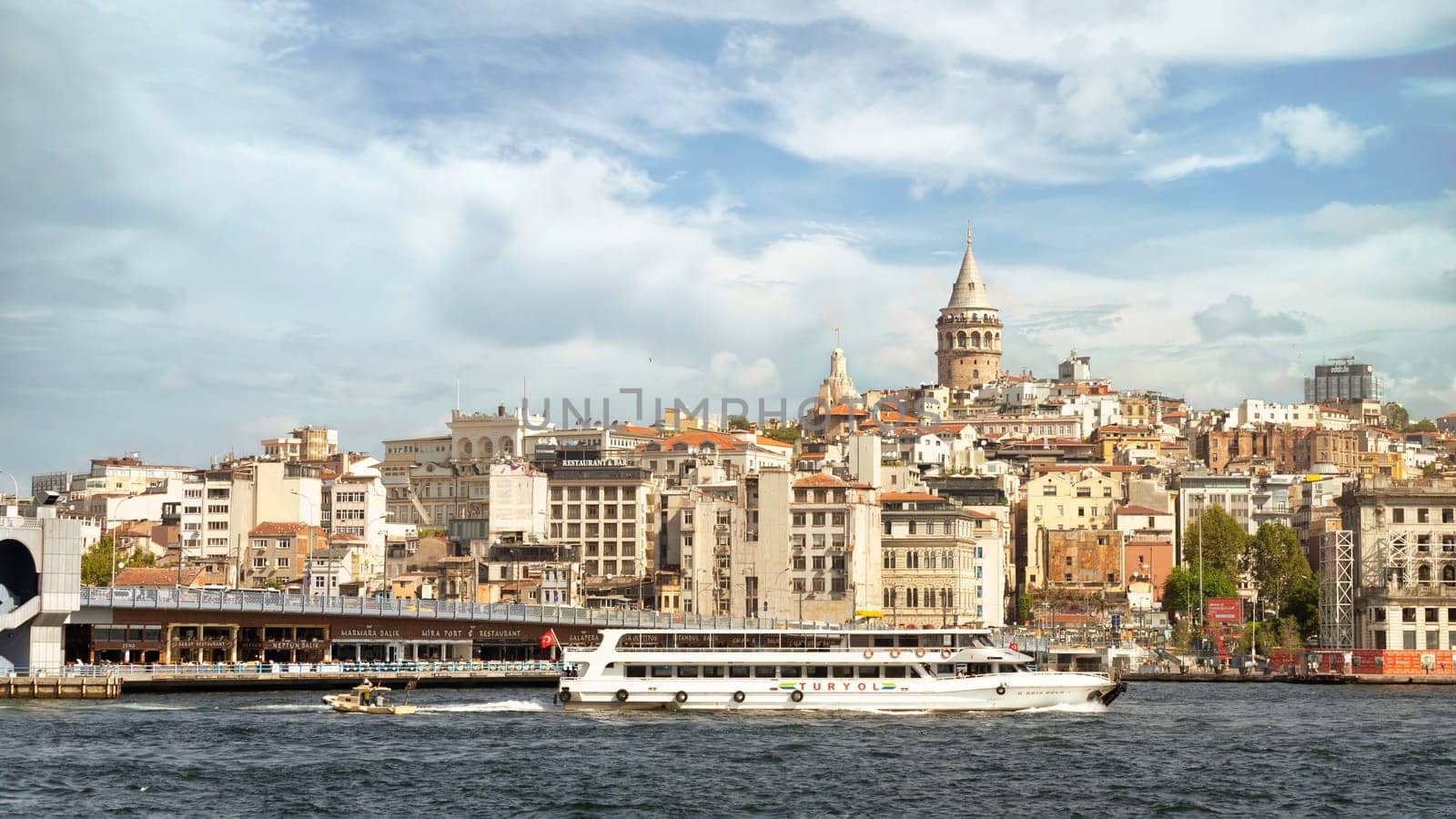 Ferry boat sailing in Bosphorus Strait, with Istanbul skyline in the background, overlooking Galata Bridge with traditional fish restaurants and Galata Tower, Istanbul, Turkey