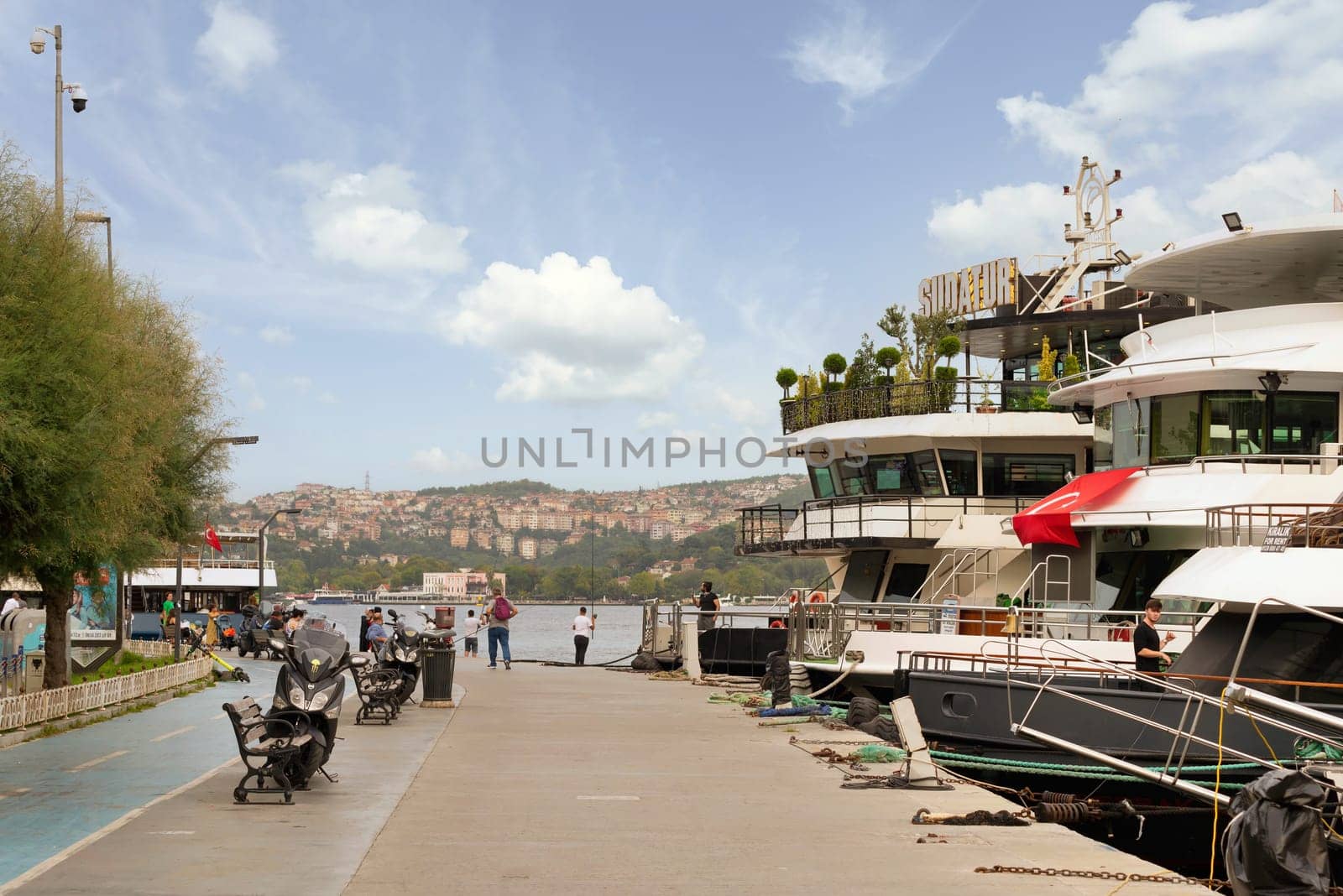 Istanbul, Turkey - August 31, 2022: Pedestrians walking on side walk by the Bosphorus Strait between Bebek and Hisari districts, beside docked boats and yachts, against clear sky on summer day