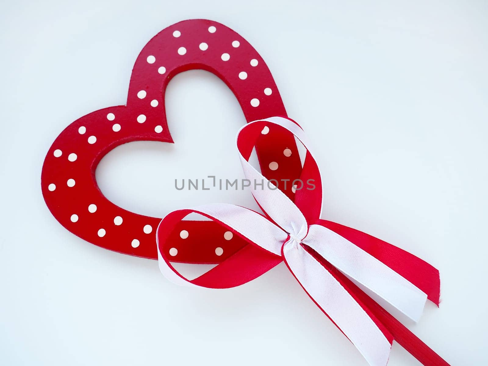 Valentine's day concept. Red wooden heart with white dots and ribbon bow on a stick. White background. A beautiful bow as a decoration. Love and relationships. Recognition or congratulations.