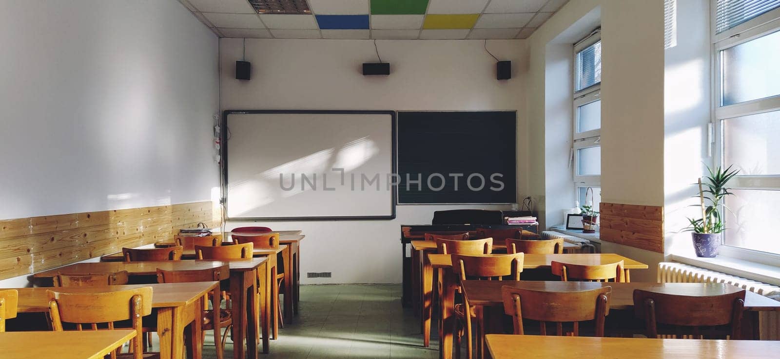 Music solfeggio empty class at school. The sun's rays fall on the floor through the window. Wooden student tables and chairs. School board and white walls. School interior