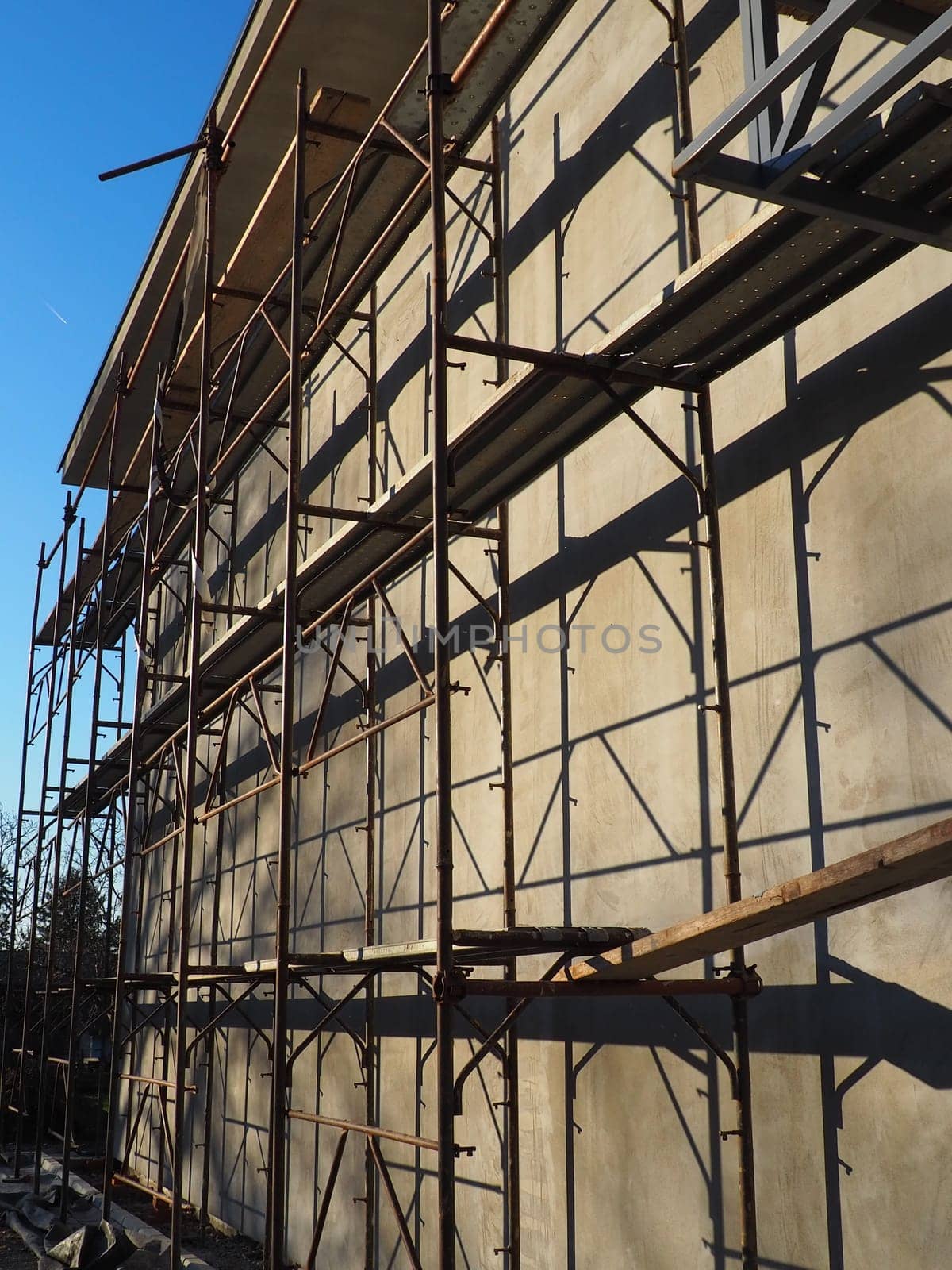 Scaffolding on a new one-story house. Facade works. Building bussiness. Low-rise private building. Plastering the wall of a building. Shop building. Metal production structures