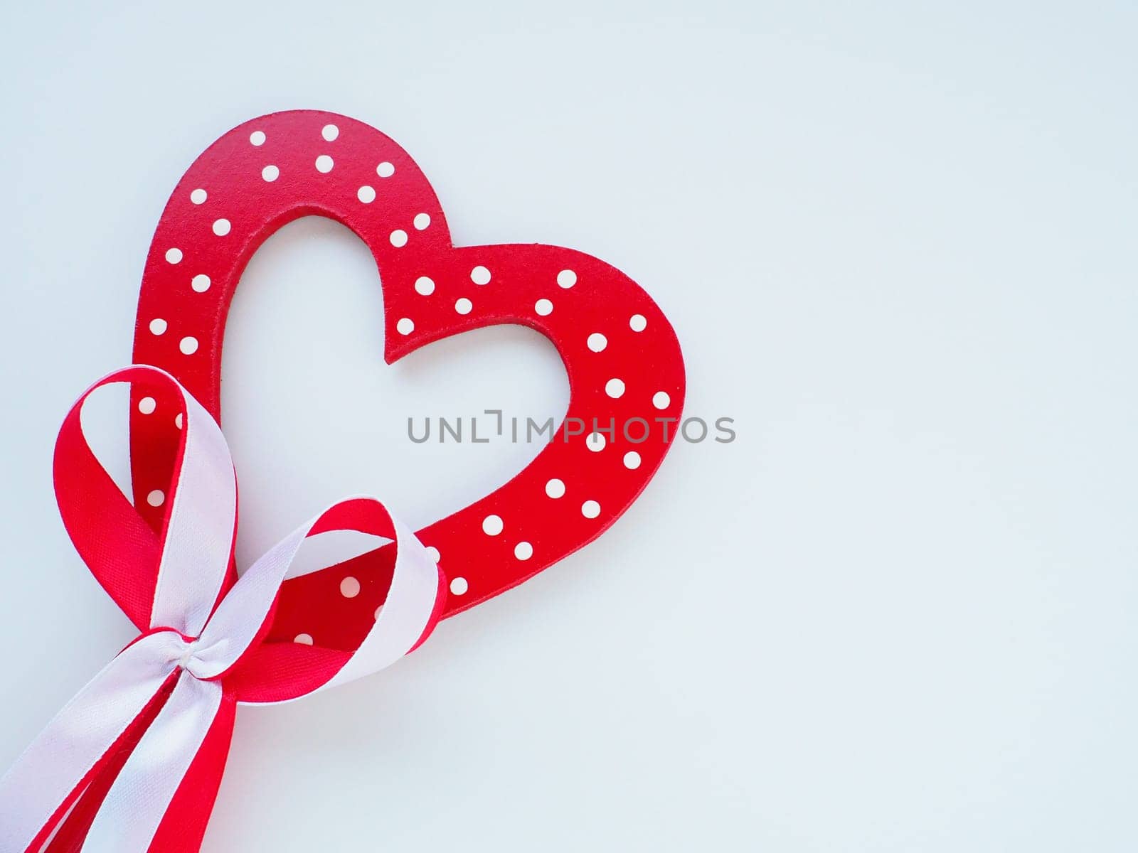 Valentine's day concept. Red wooden heart with white dots and ribbon bow on a stick. White background. A beautiful bow as a decoration. Love and relationships. Recognition or congratulations.