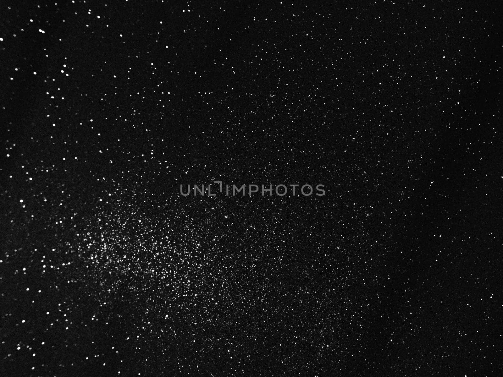Black bokeh texture on black background. White glitter or illuminated dust.