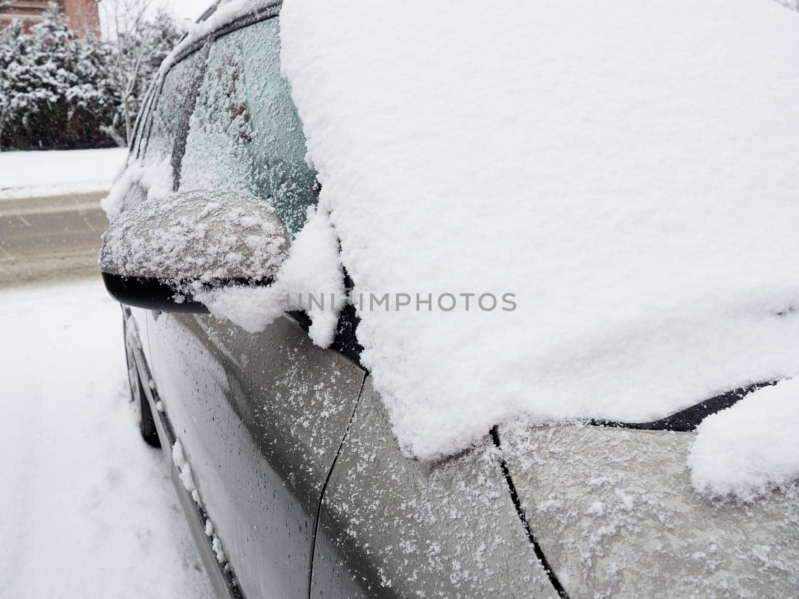 Snow and ice on the windshield, retrovisors and rear-view mirrors of the car. Winter driving conditions. Snow cleaning. Road traffic in winter. Metallic car. Snowdrifts and slush