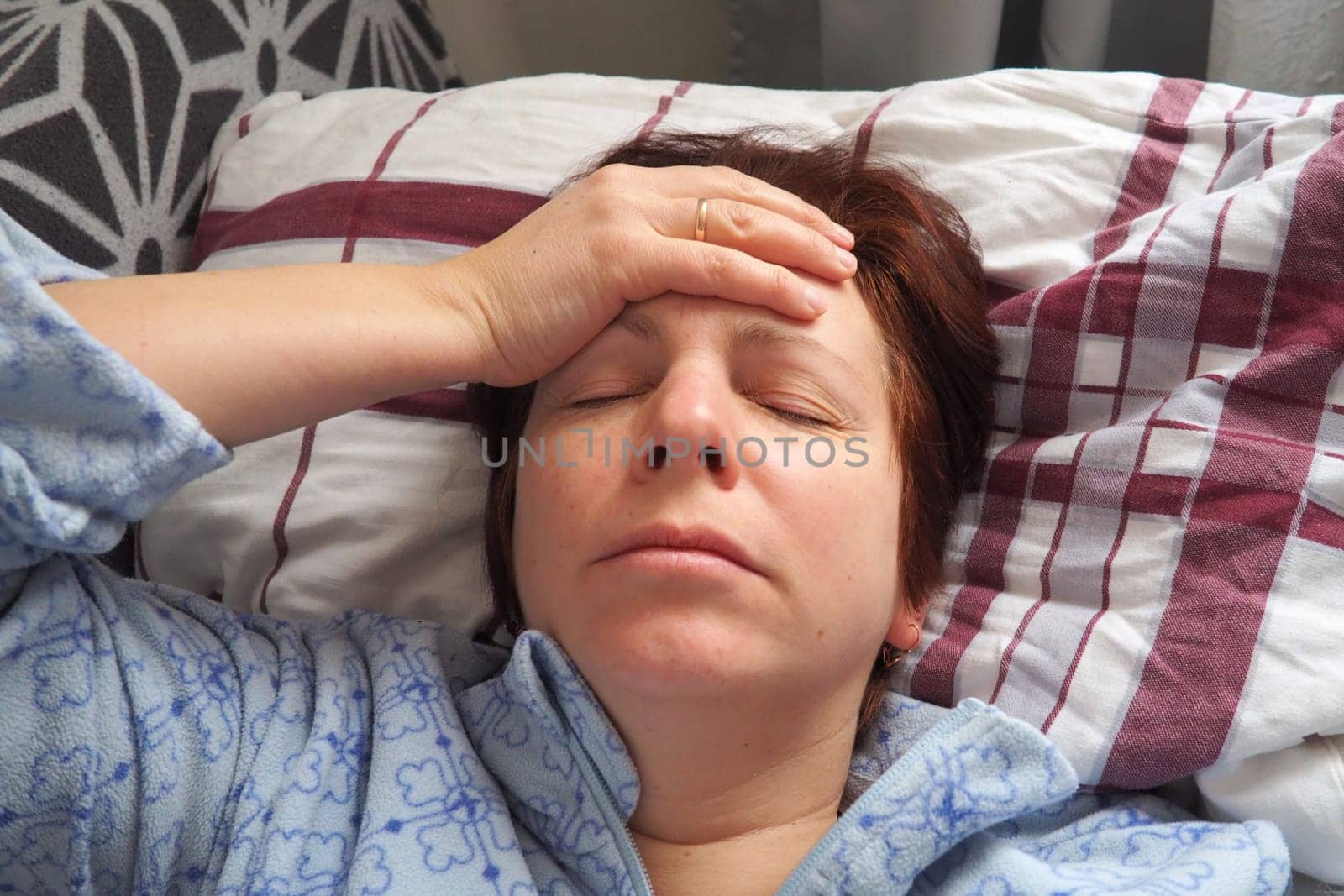 Sick woman in bed. Headache, runny nose and cold. Paleness of the face and faintness of the body. Feeling unwell. The patient holds his forehead with his hand and covers his eyes.