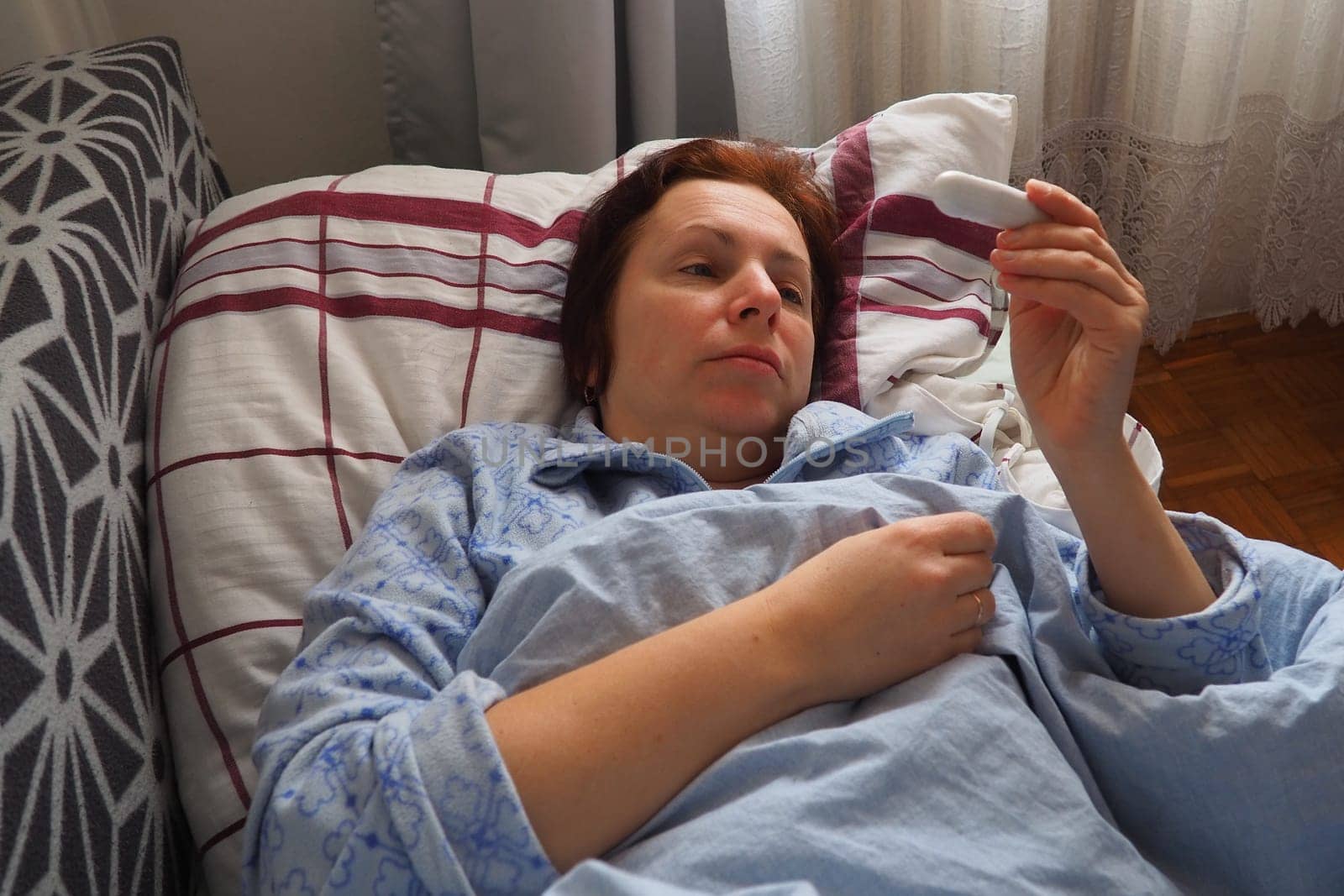 Sick woman in bed. Headache, runny nose and cold. Paleness of the face and faintness of the body. Feeling unwell. The patient lies on a pillow, holds a thermometer and measures the temperature