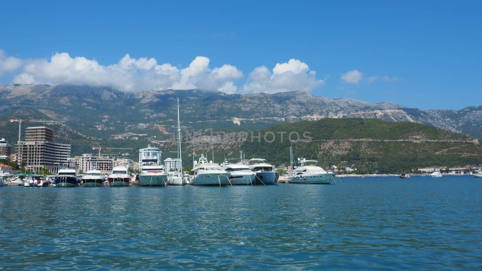 Budva, Montenegro, August 15 2022 Adriatic sea, coast, mountains, sea ripples. Boats and ships are moored to the embankment. Water transport parking. Summer resort trips with tourist water activities.