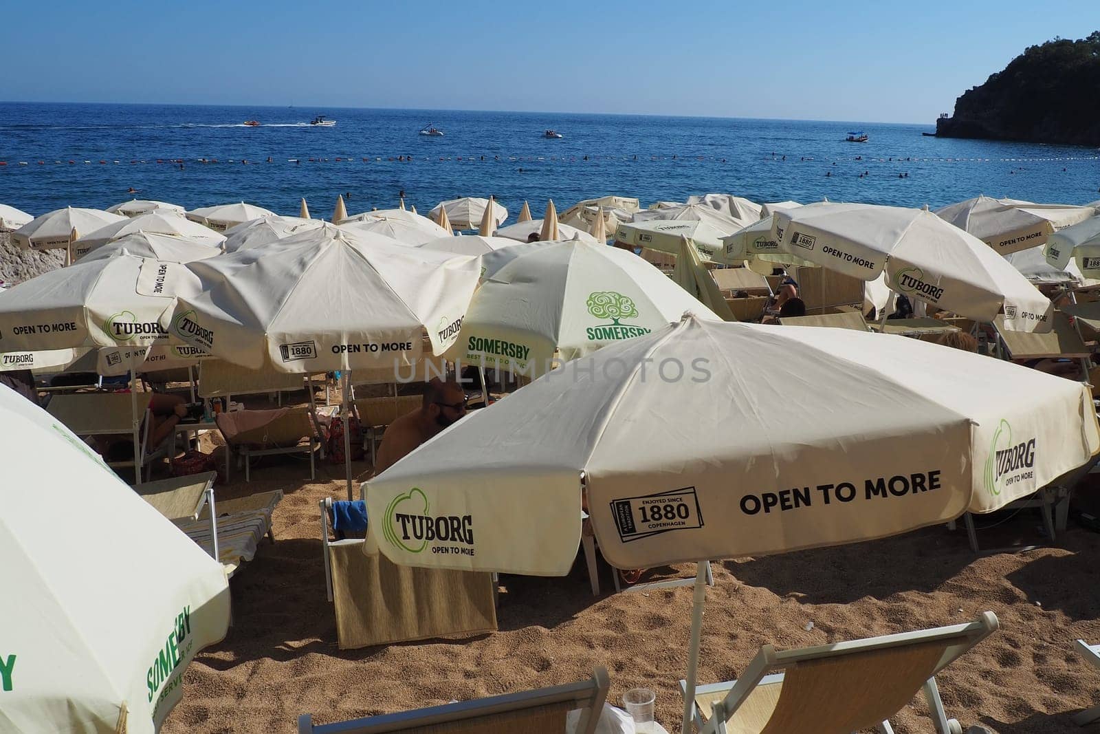 Budva, Montenegro, Mogren beach. August 15 2022 Sand and pebble beach near high cliffs. Beach umbrellas, cafes, deck chairs. People relax, swim, enjoy and sunbathe. Tourism business in the Balkans