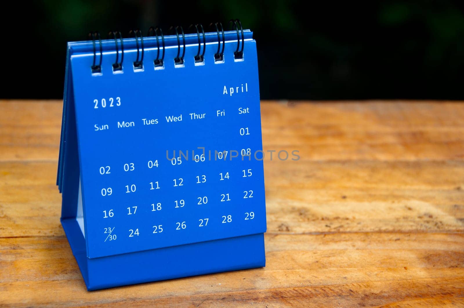 April 2023 blue desk calendar on wooden table background with customizable space for text.