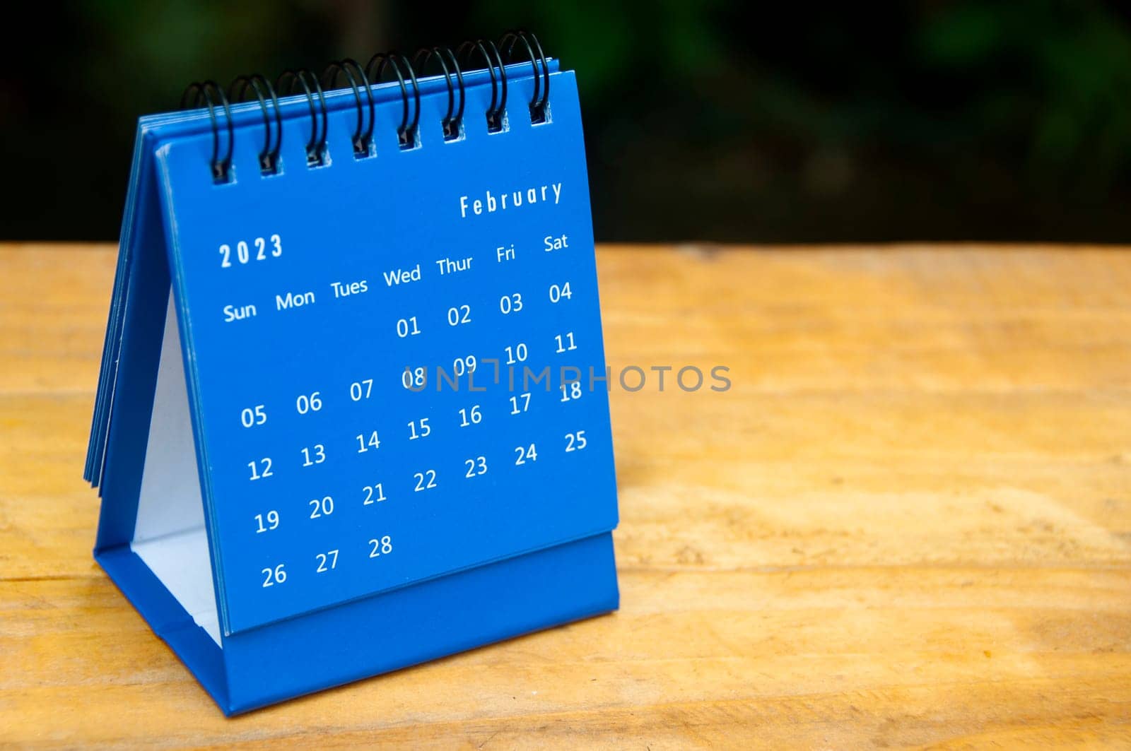 February 2023 blue desk calendar on wooden table background with customizable space for text.