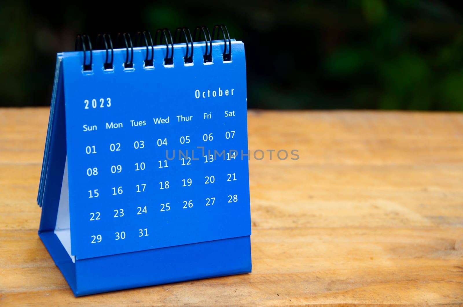October 2023 blue desk calendar on wooden table background with customizable space for text.