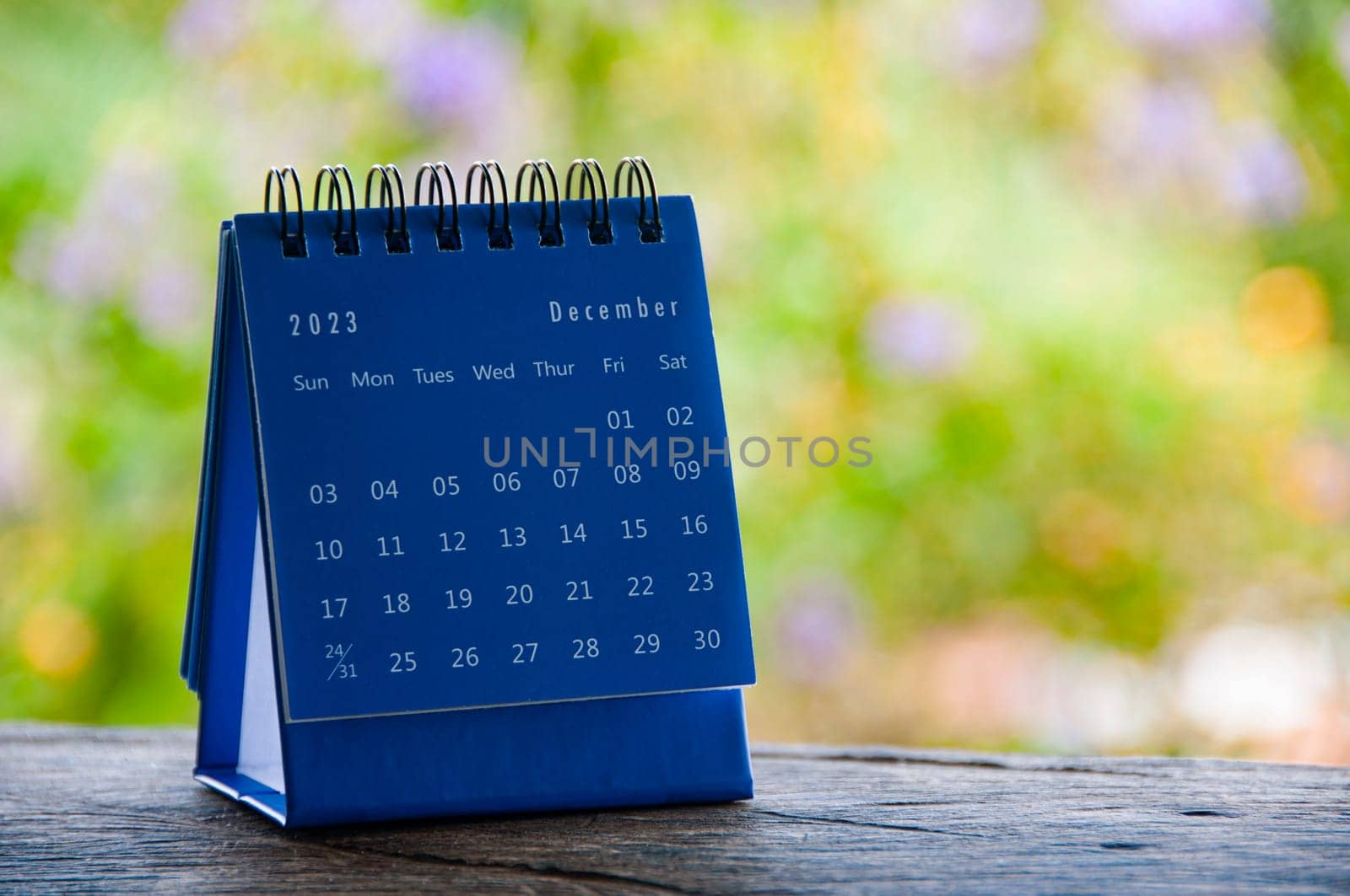 December 2023 blue desk calendar with blurred nature with customizable space for text.