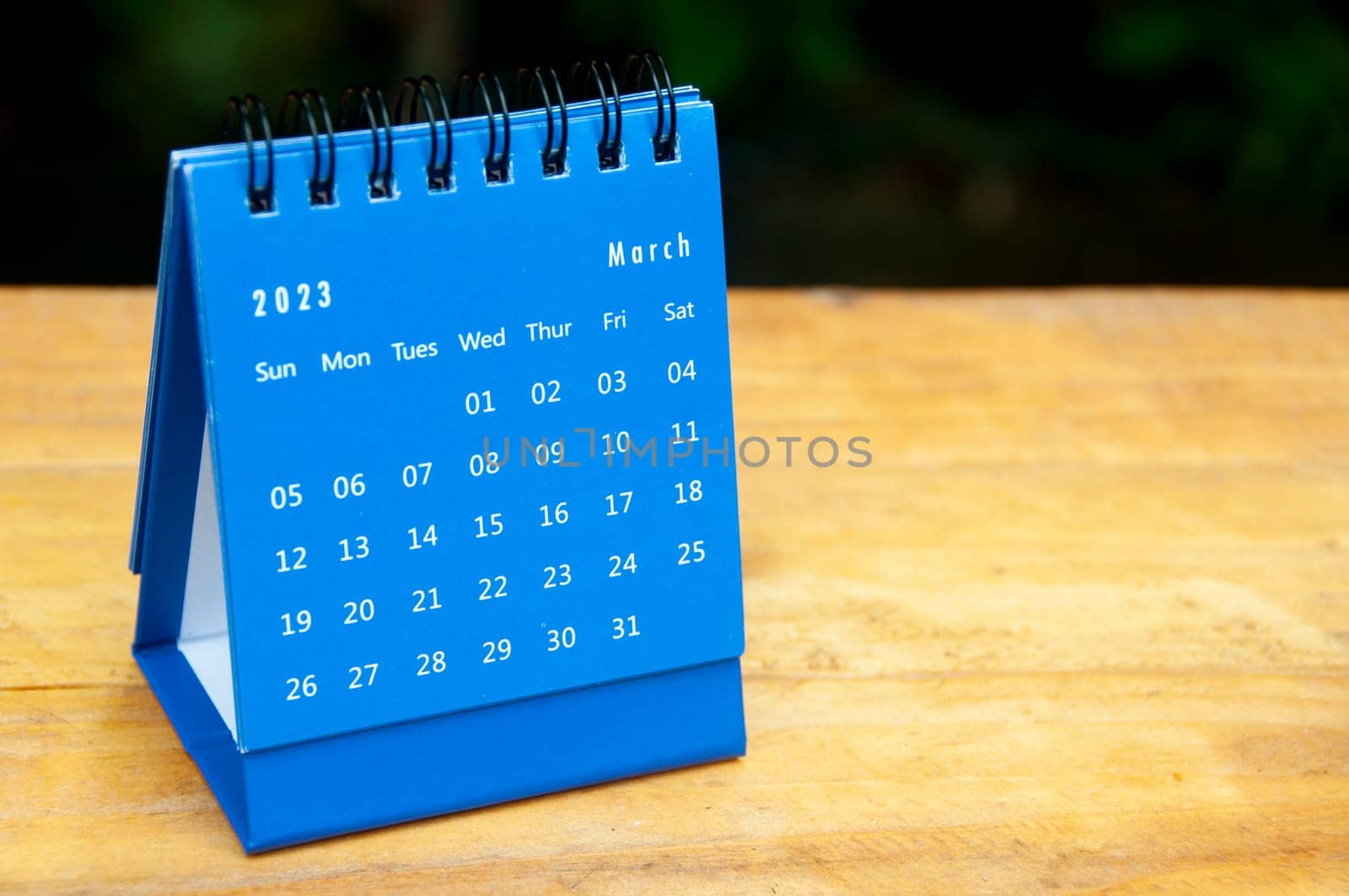 March 2023 blue desk calendar on wooden table background with customizable space for text.