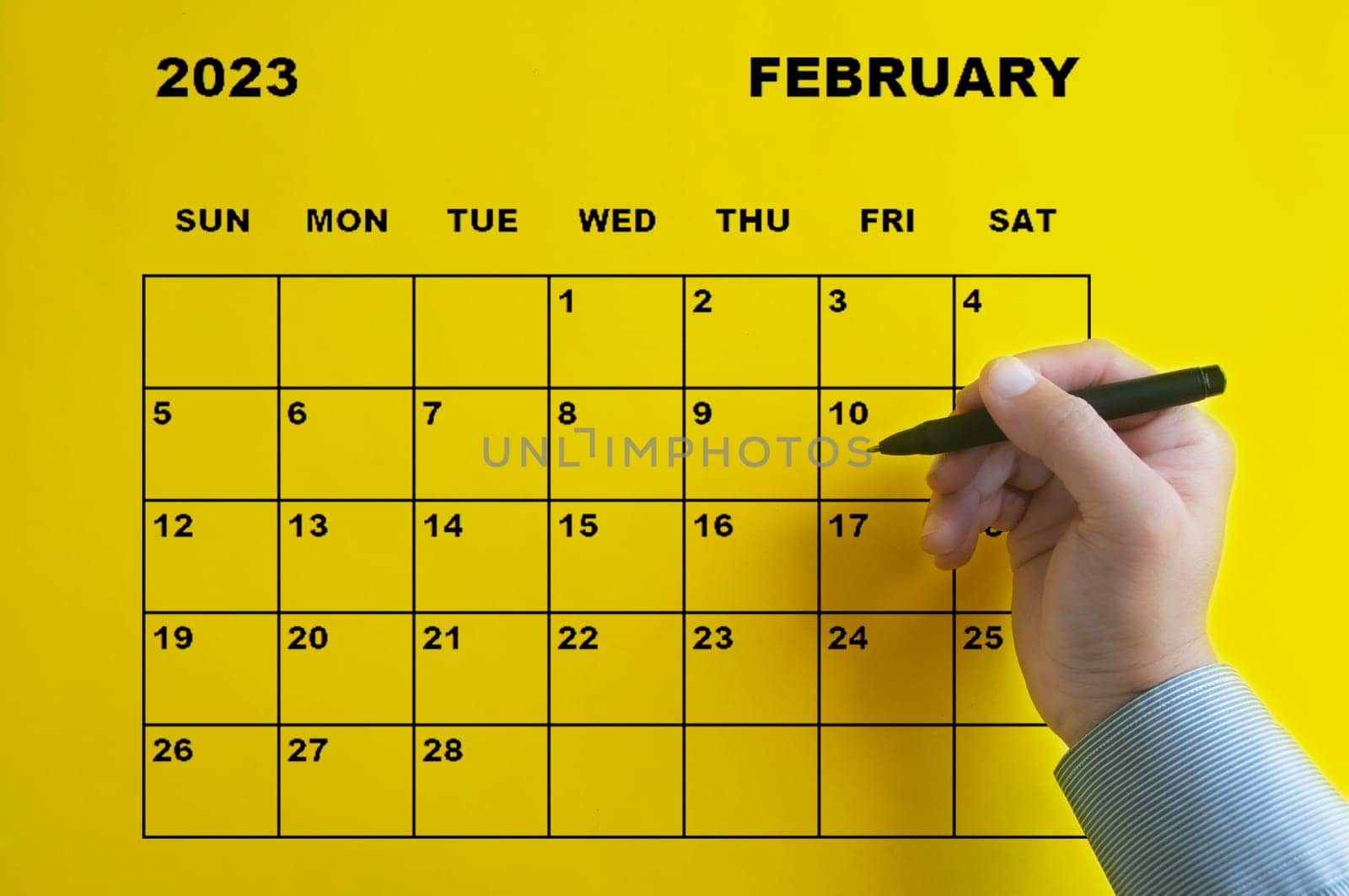 February 2023 calendar with hand holding black pen on yellow background. Appointment concept
