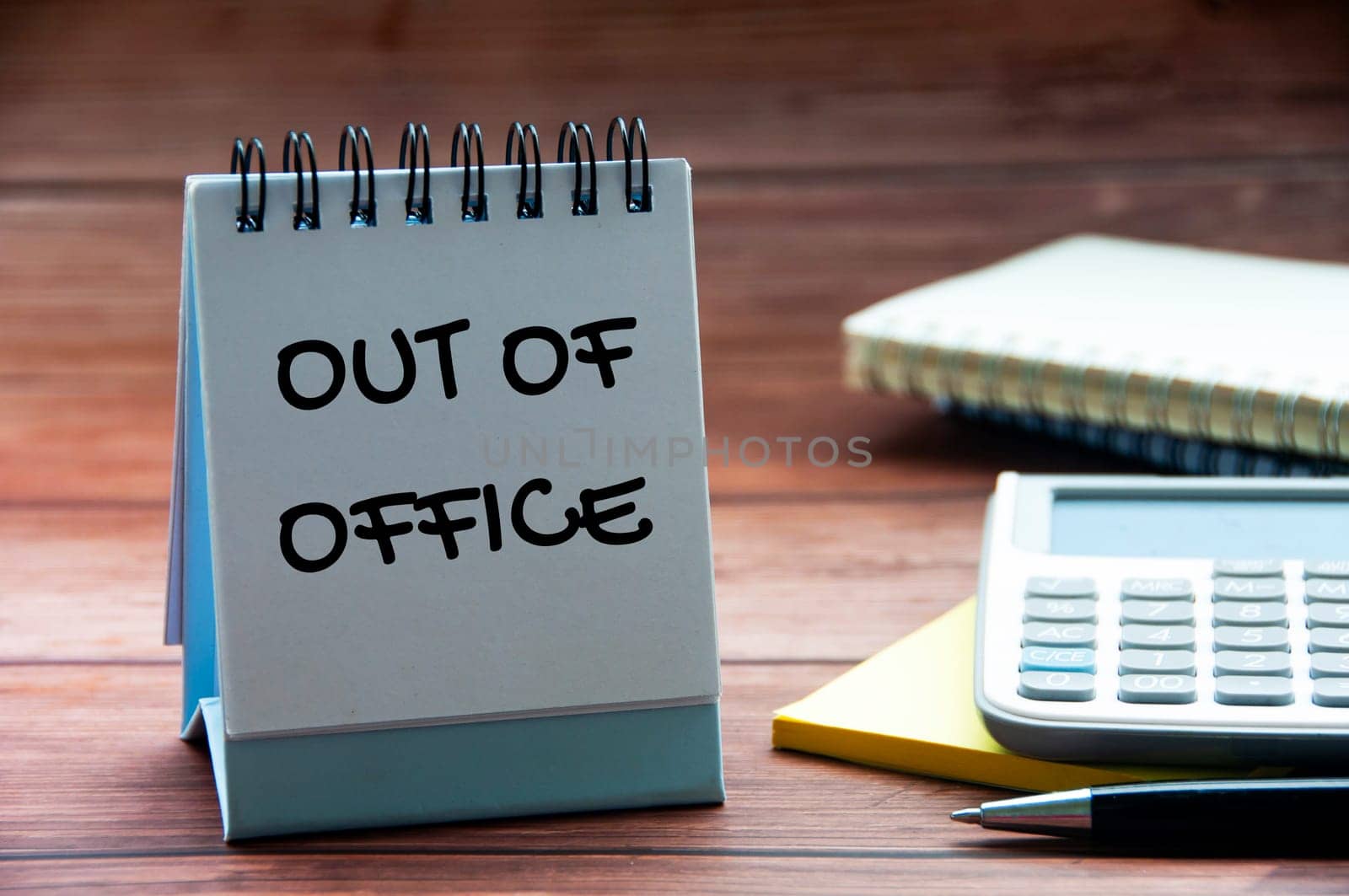 Out of office text on calendar desk with notebook, calculator and pen background. Out of office concept
