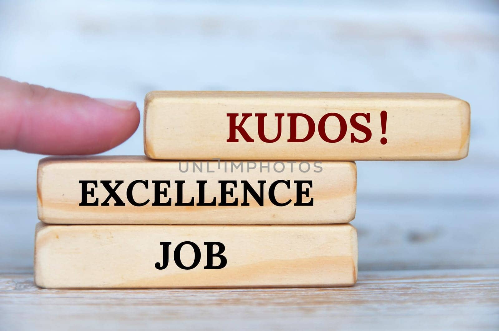 Finger pointing KUDOS text on wooden blocks with wooden cover background. Achievement concept.