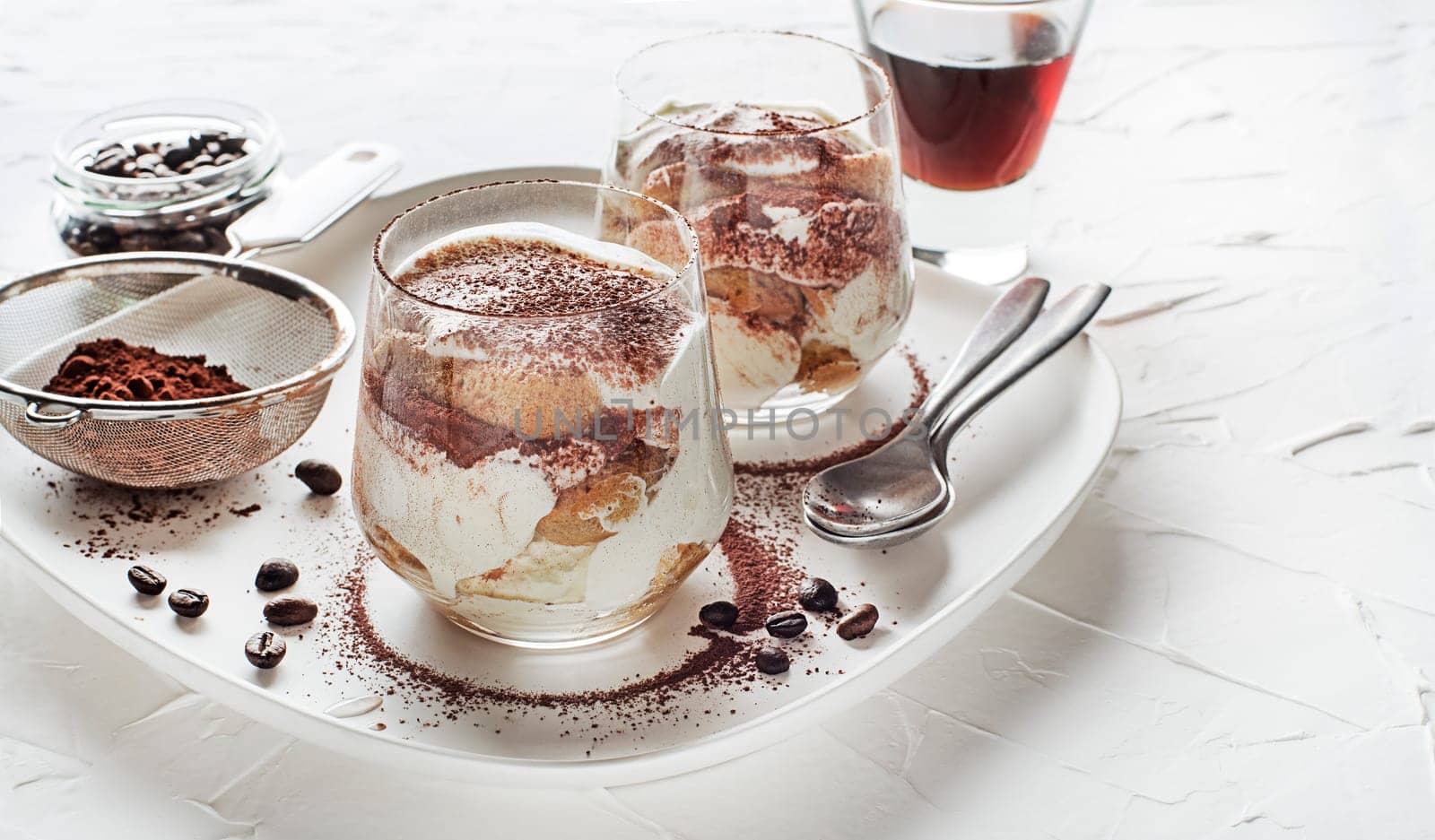 Traditional Italian dessert tiramisu in a glass cup. Homemade tiramisu in glass cup, step by step cooking process. Traditional unbaked Italian dessert on white background. Coffee and mascarpone cream
