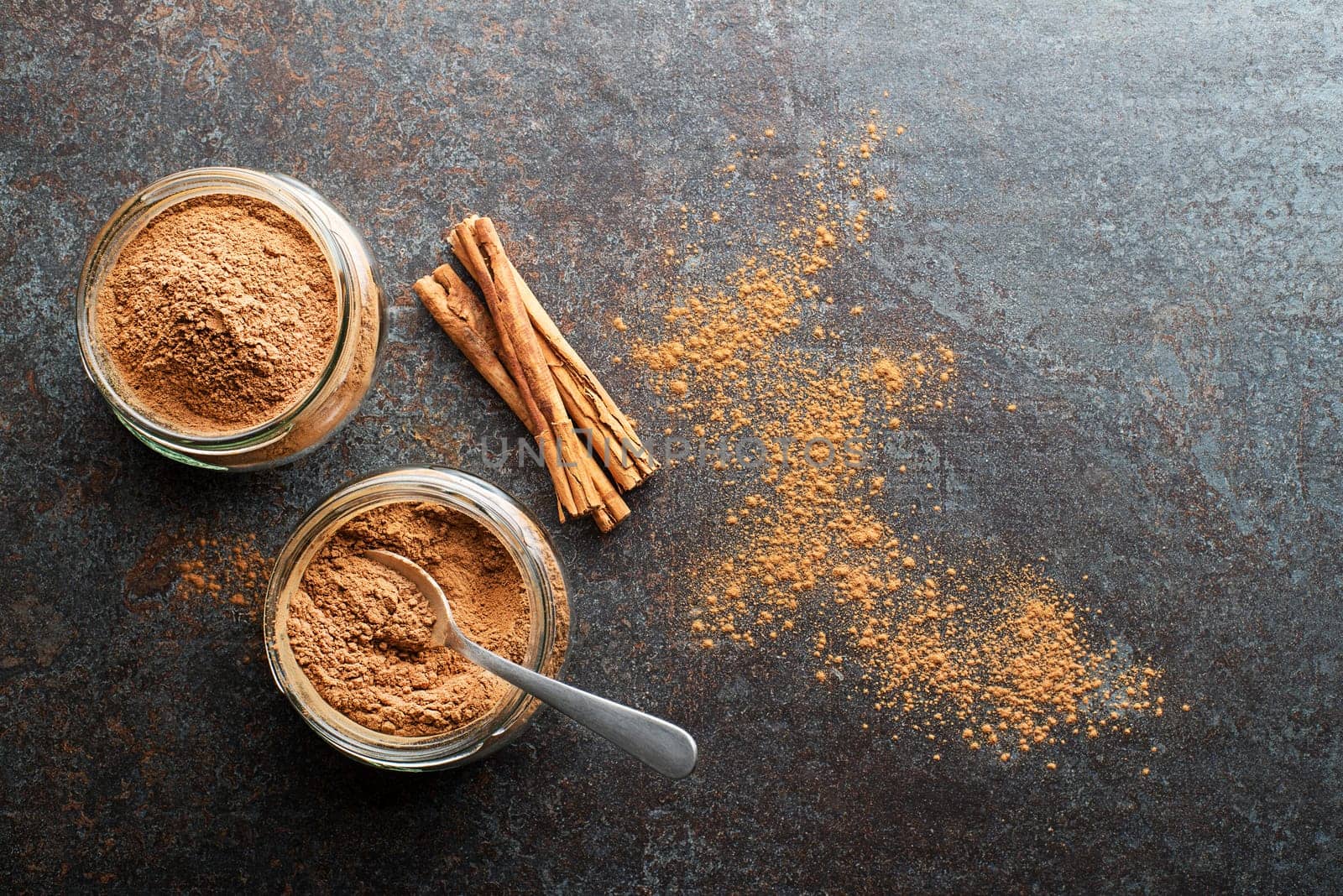 Ground cinnamon in glass cups and cinnamon sticks with powder on grey rustic background