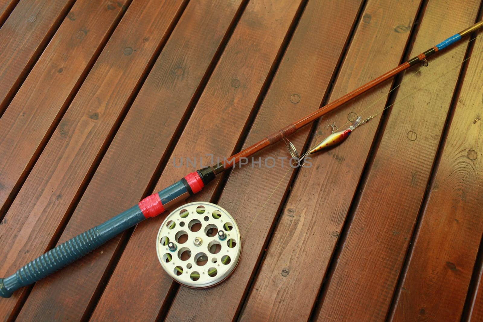 vintage fishing rod with a big reel and a wobbler on a wooden background