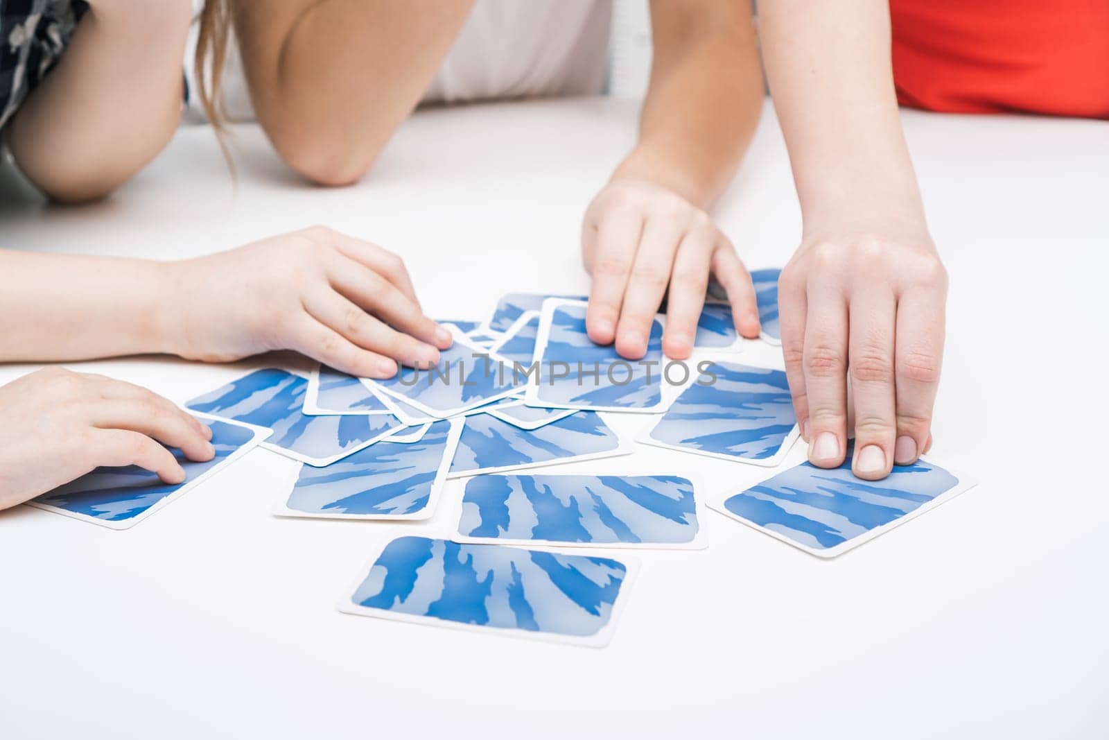 Cropped photo of group of children playing board game card game geistes blitz on white table, touching choosing blue card face down. Board games, development, education, entertainment, free time.