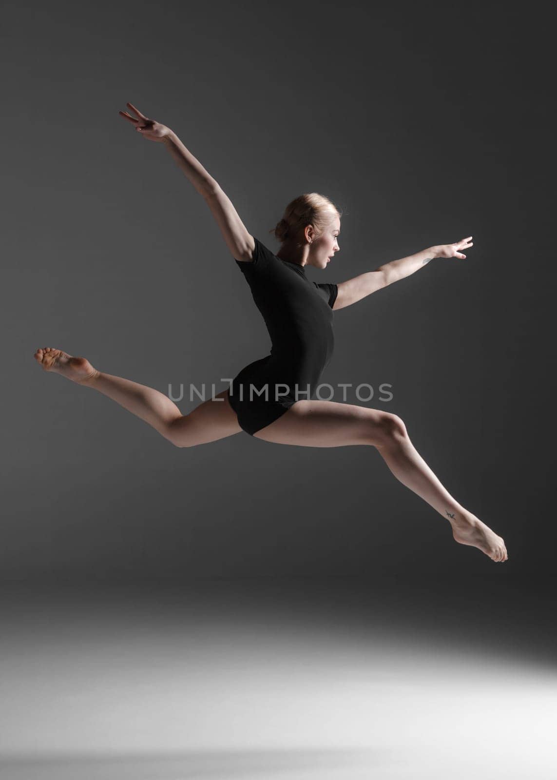 young beautiful modern style dancer jumping on a studio gray background