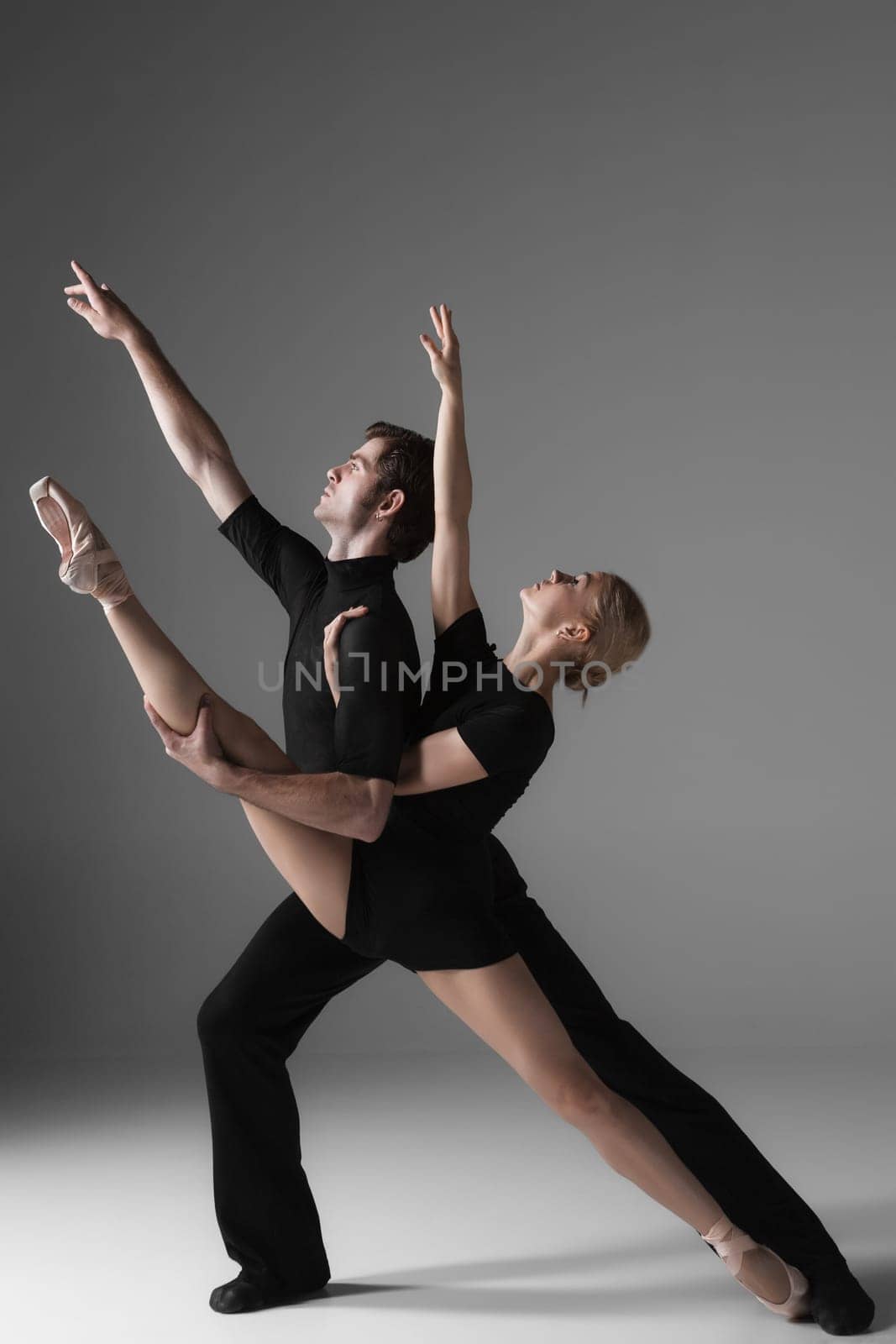 The two young modern ballet dancers in black suits posing over gray studio background