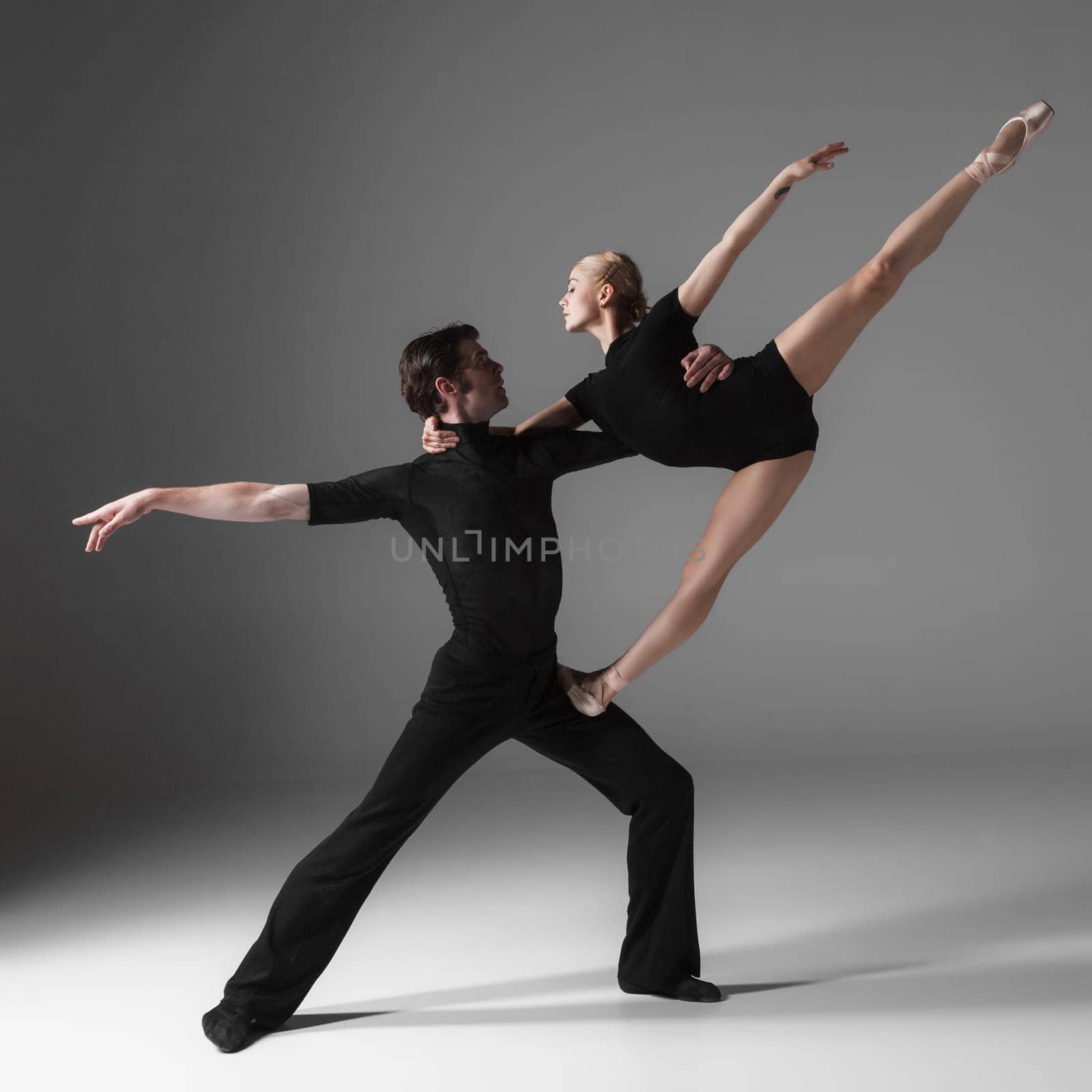 The two young modern ballet dancers in black suits posing over gray studio background