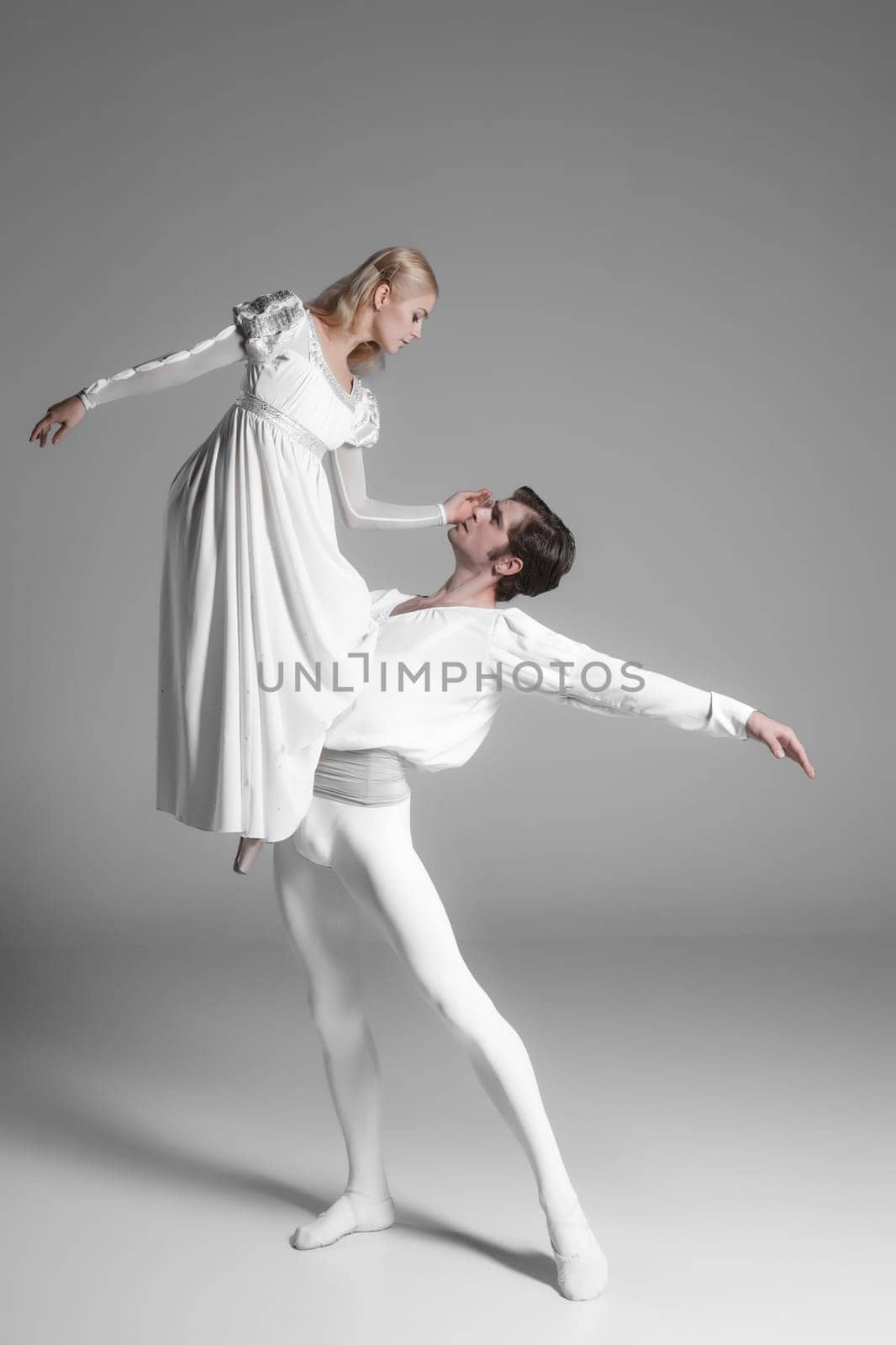 Two young classic ballet dancers practicing. attractive dancing performers  in white suits over gray background