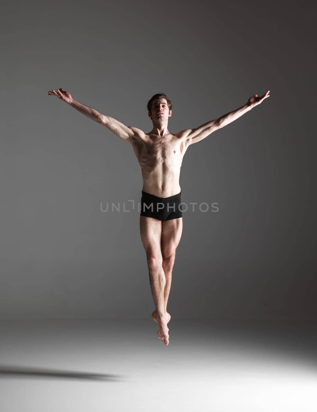 The young attractive modern ballet dancer jumping over gray background