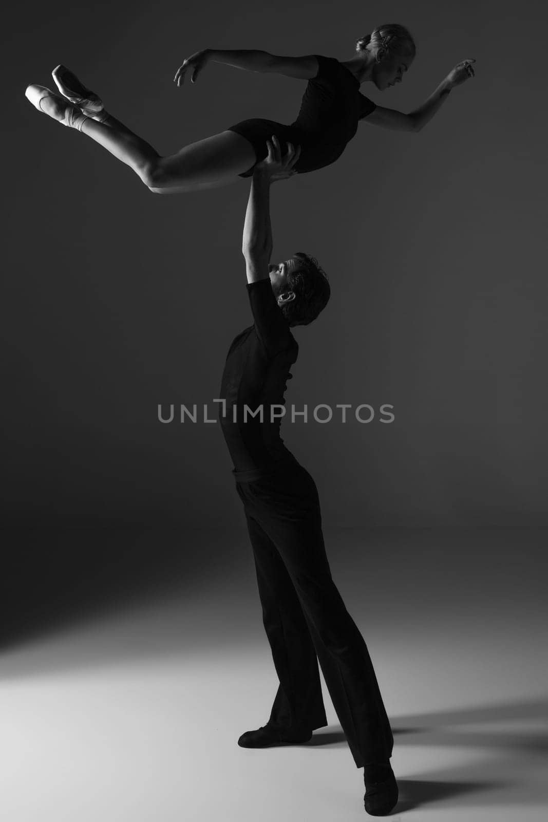 The two young modern ballet dancers in black suits posing over gray studio background