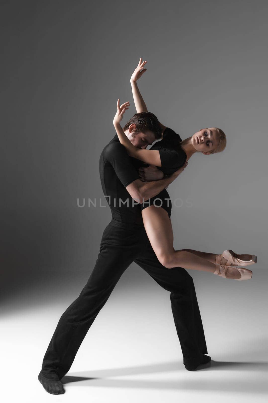 The two young modern ballet dancers in black suits posing over gray studio background
