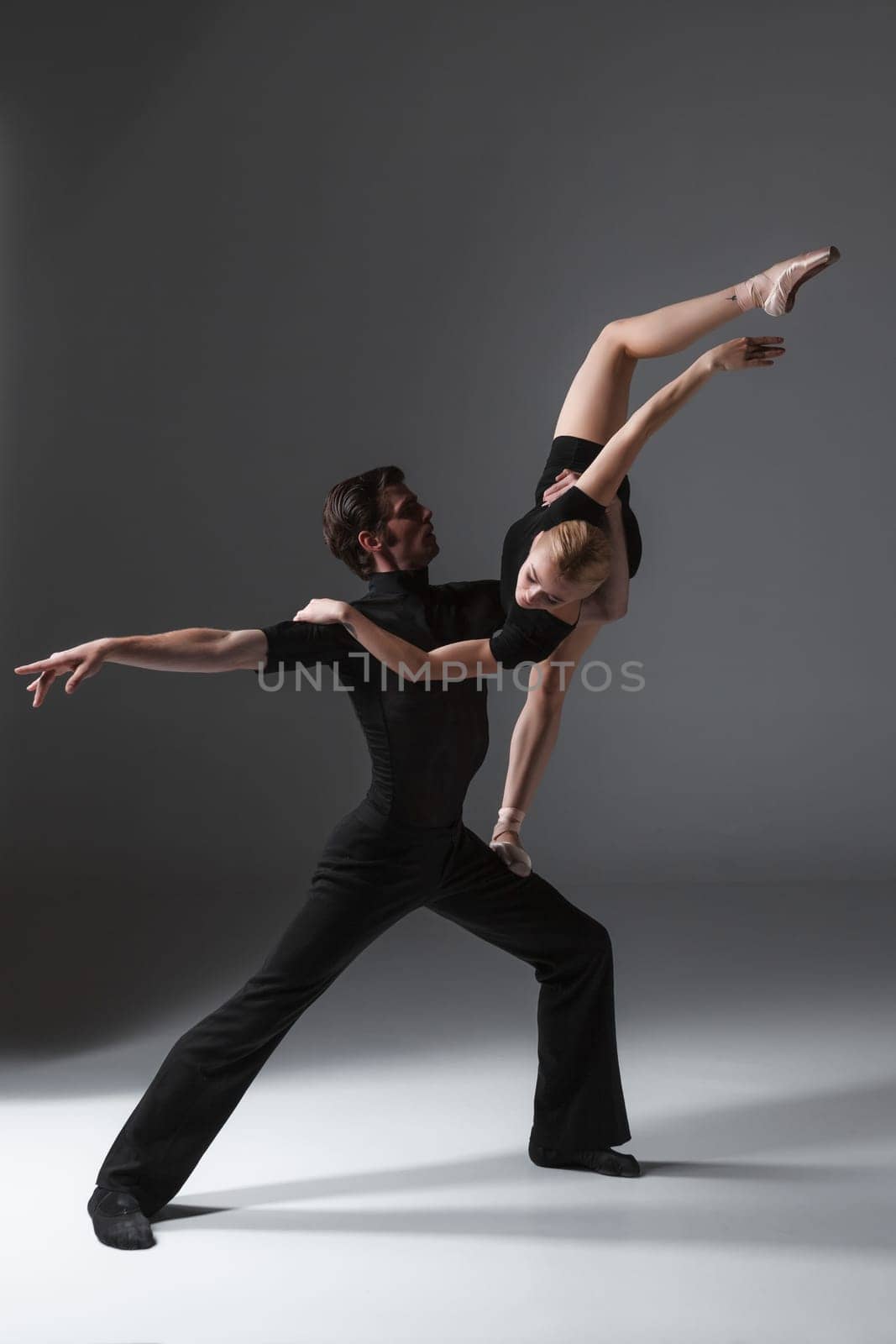 The two young modern ballet dancers in black suits posing over gray studio background