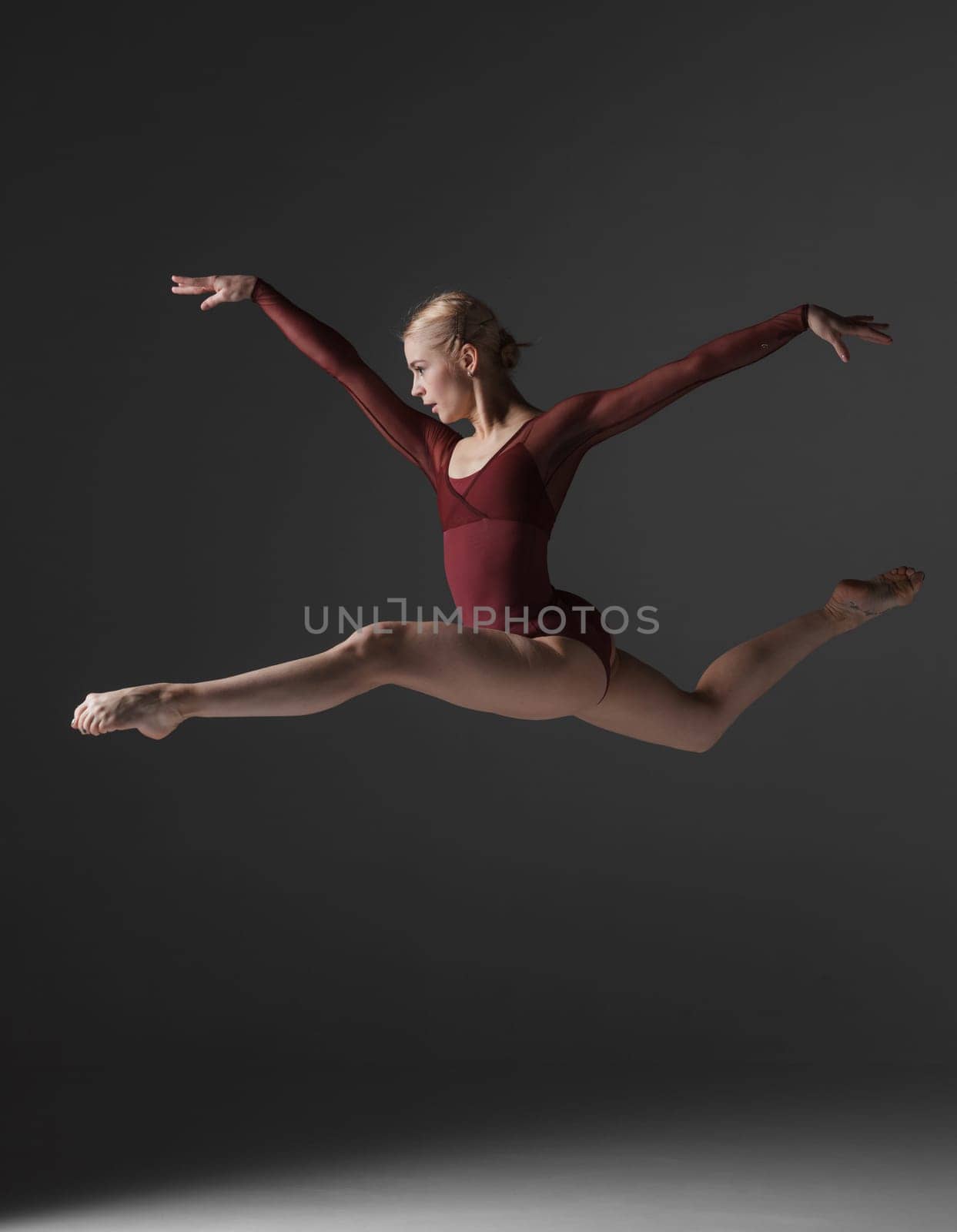 young beautiful modern style dancer jumping on a studio gray background