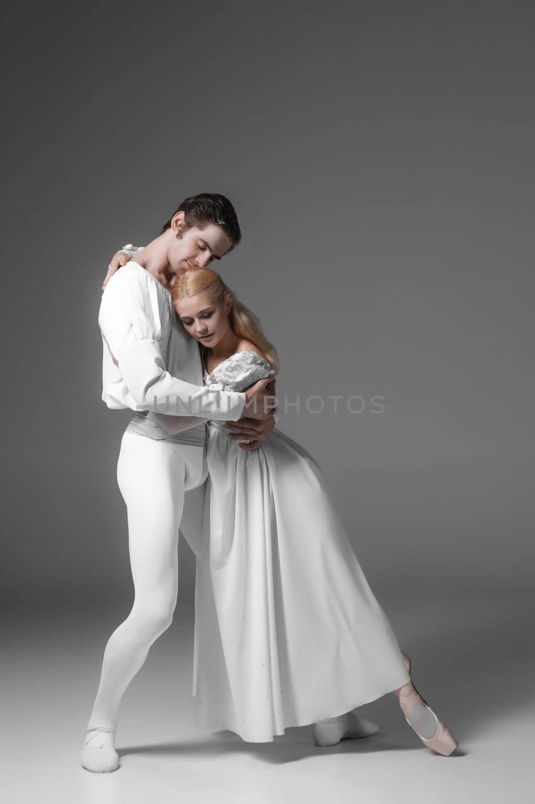 Two young classic ballet dancers practicing. attractive dancing performers  in white suits over gray background