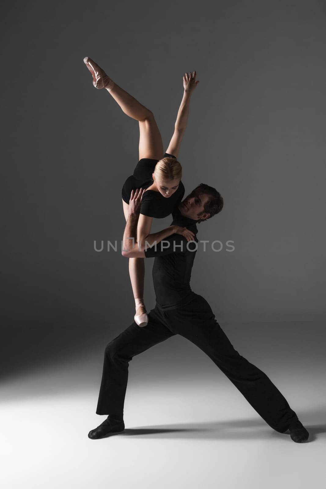 The two young modern ballet dancers in black suits posing over gray studio background