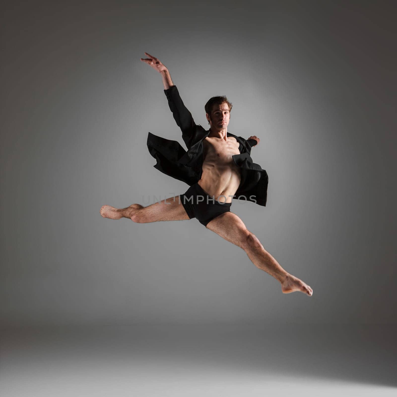 The young attractive modern ballet dancer in black jacket  jumping over gray background
