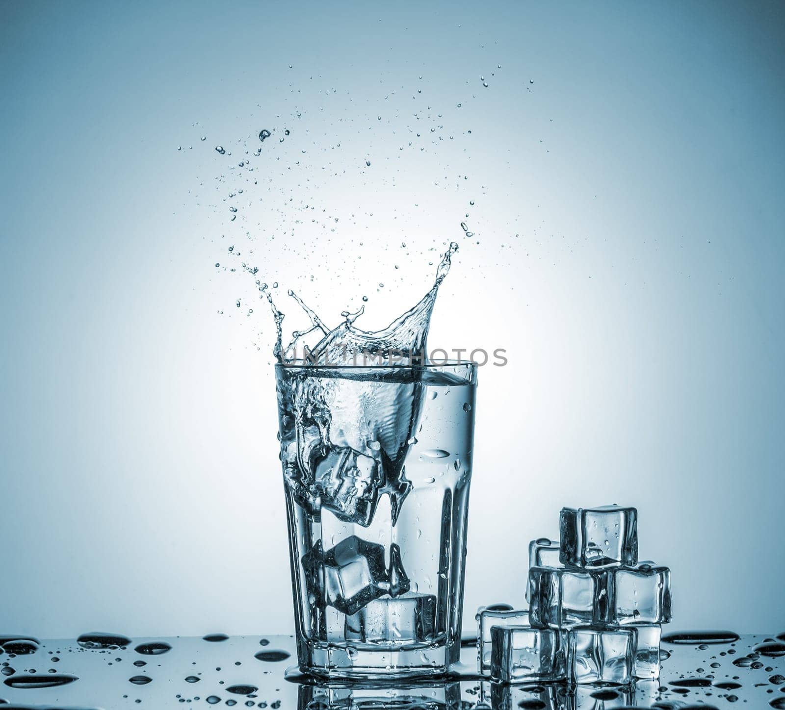 ice cubes falling into a glass of water and ice cubes, lying next, on blue background