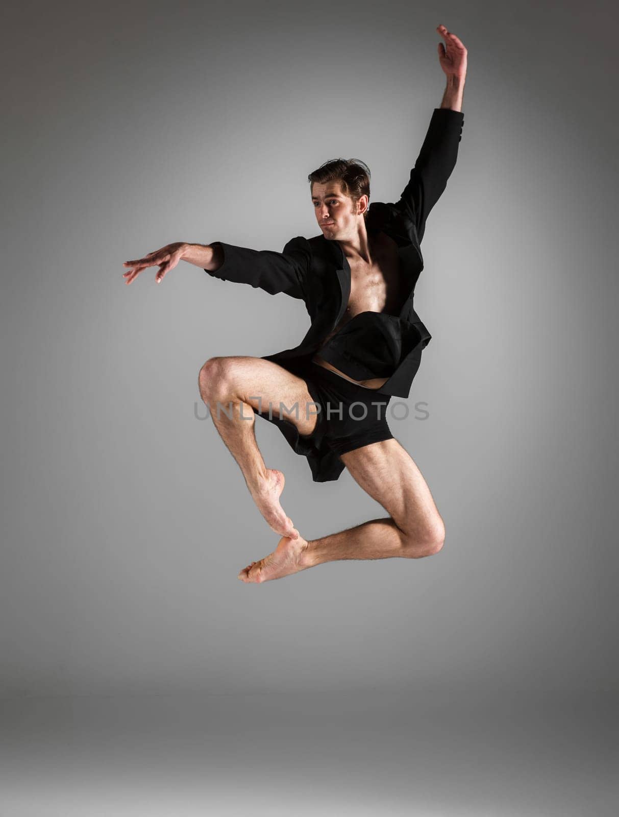 The young attractive modern ballet dancer in black jacket  jumping over gray background