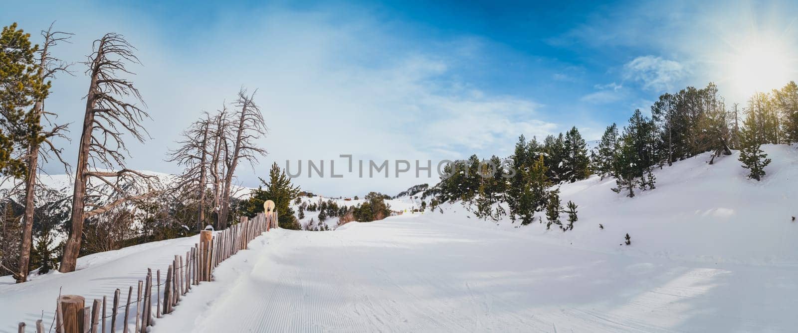 Fresh snow covering ski piste with beautiful view on snowy mountains and green pine forest on a sunny day in Andorra, El Tarter, Pyrenees Mountain