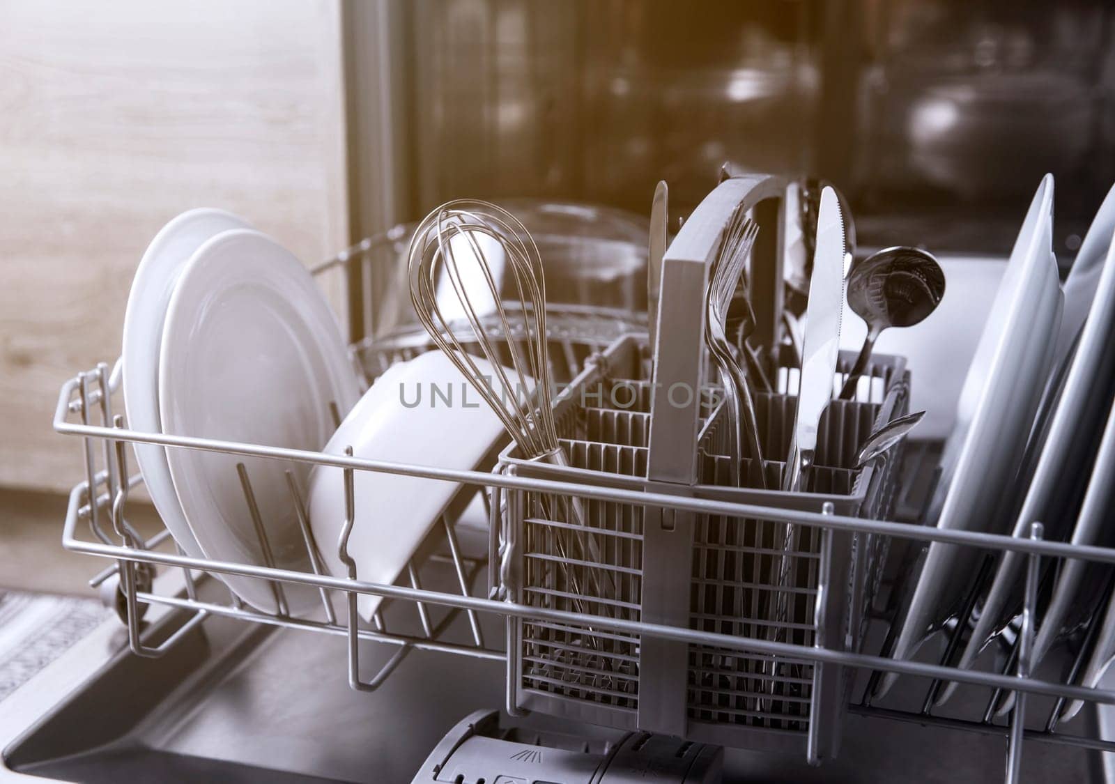 Front view of open automatic stainless steel built-in fully integrated top control dishwasher range machine with clean utensils, cutlery, glasses, dishes, plates inside in modern home kitchen
