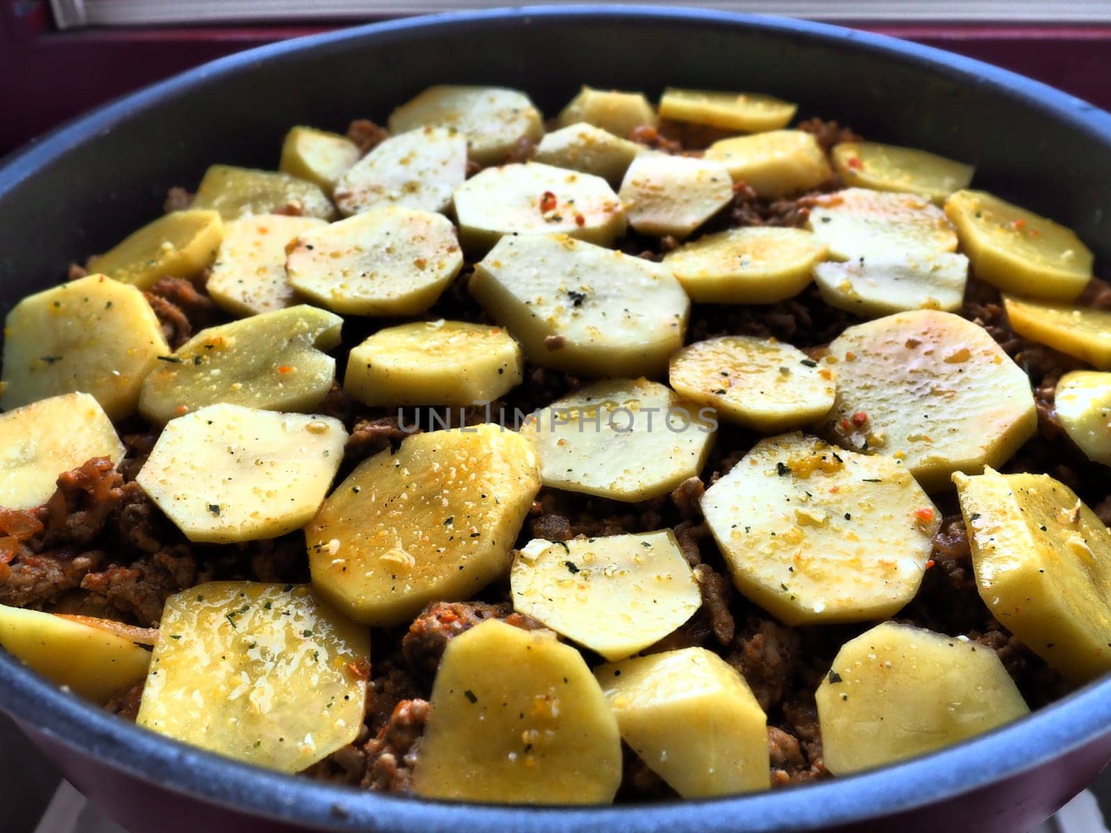 Raw potatoes, cut into circles and stacked on top of minced meat and onions. Moussaka making process. Spices on potatoes. Balkan cuisine - traditional Greek, Serbian and Turkish food.