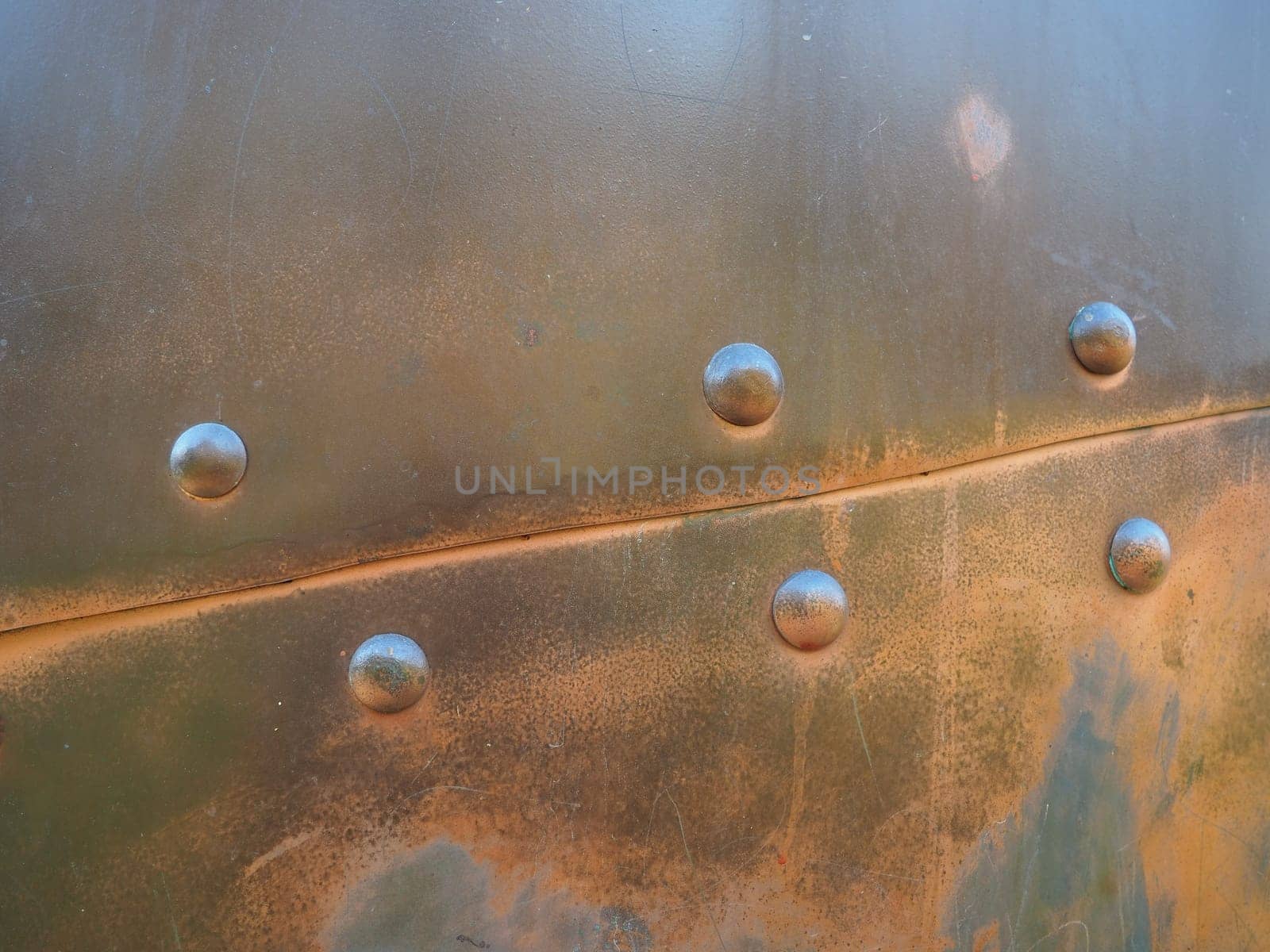 Metal surface with rivets and bolts. Abstract background of a military or industrial nature. Sheathing with dents, seams and nuts. Fasteners on metal. Steel or bronze panel.