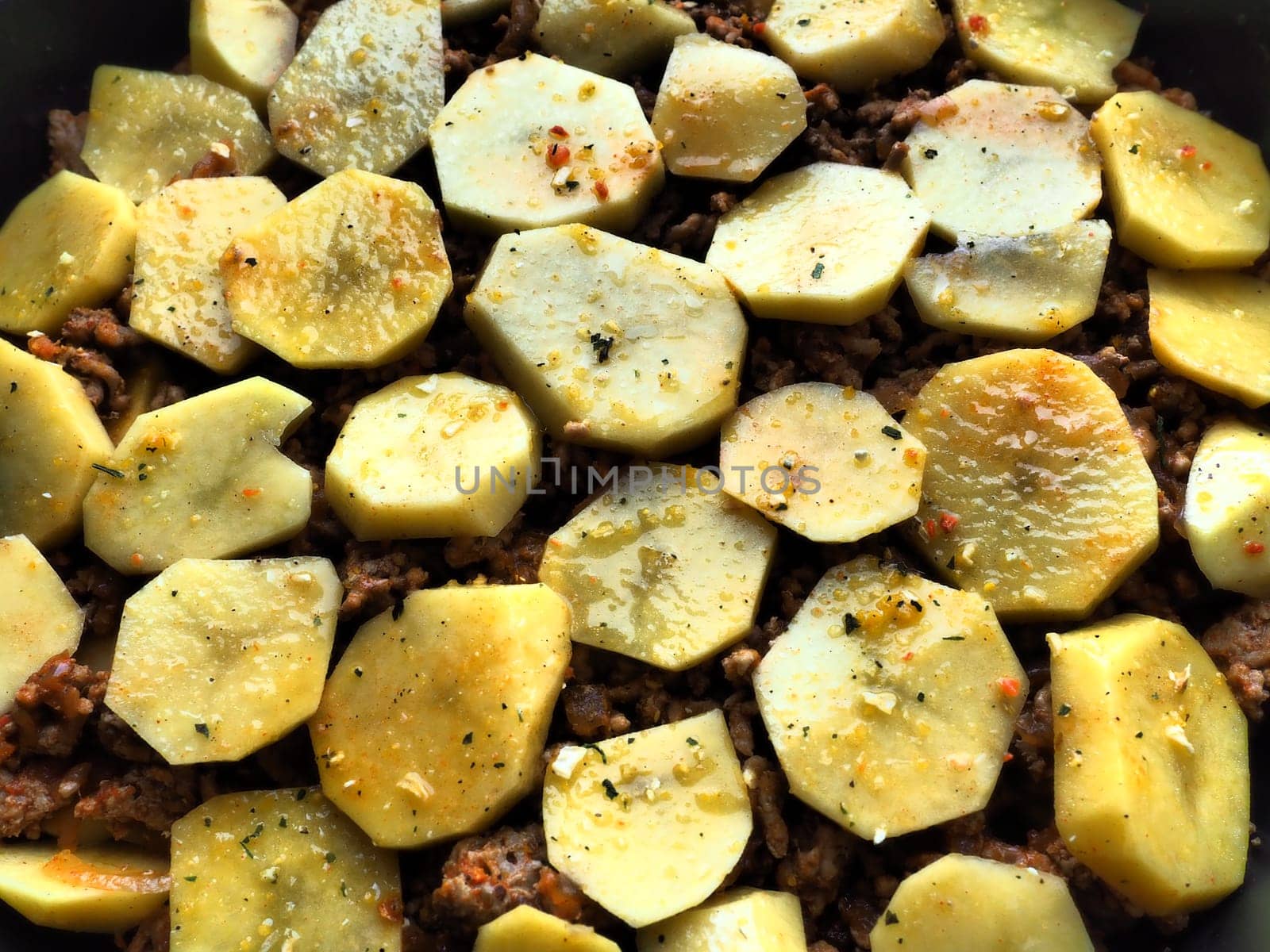 Raw potatoes, cut into circles and stacked on top of minced meat and onions. Moussaka making process. Spices on potatoes. Balkan cuisine - traditional Greek, Serbian and Turkish food.