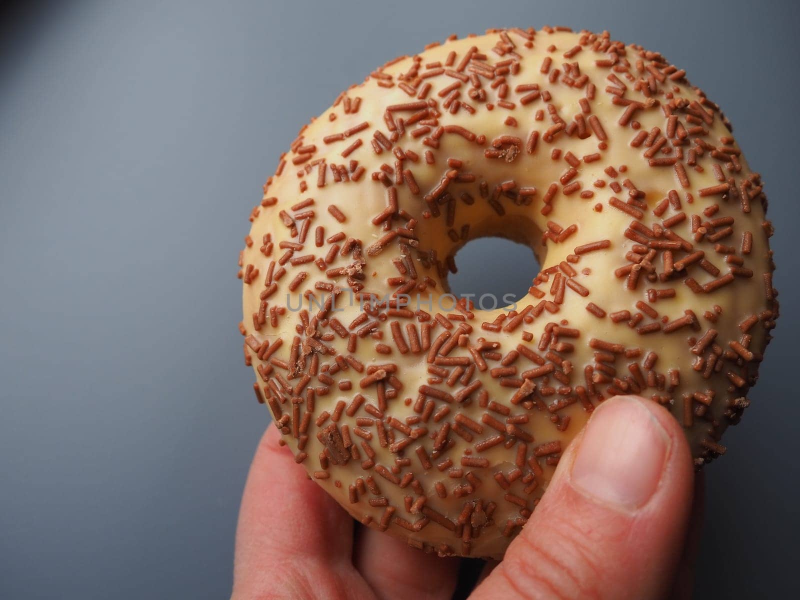 A doughnut or donut. A type of leavened fried dough. Sweet snack that can be homemade or purchased in bakeries, supermarkets, food stalls. Delicious pie with light icing on a gray background in hand.