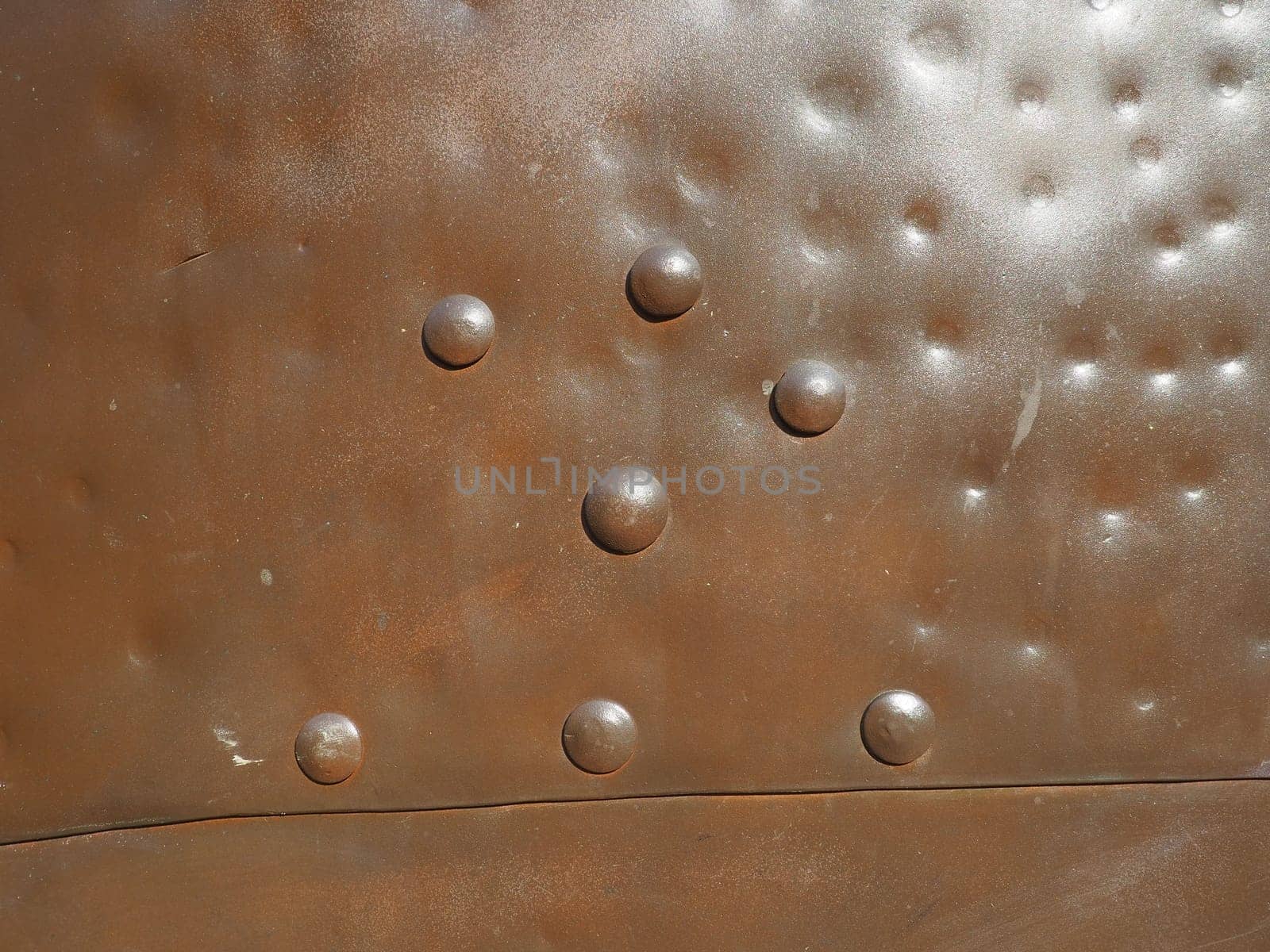 Metal surface with rivets and bolts. Abstract background of a military or industrial nature. Sheathing with dents, seams and nuts. Fasteners on metal. Steel or bronze panel.