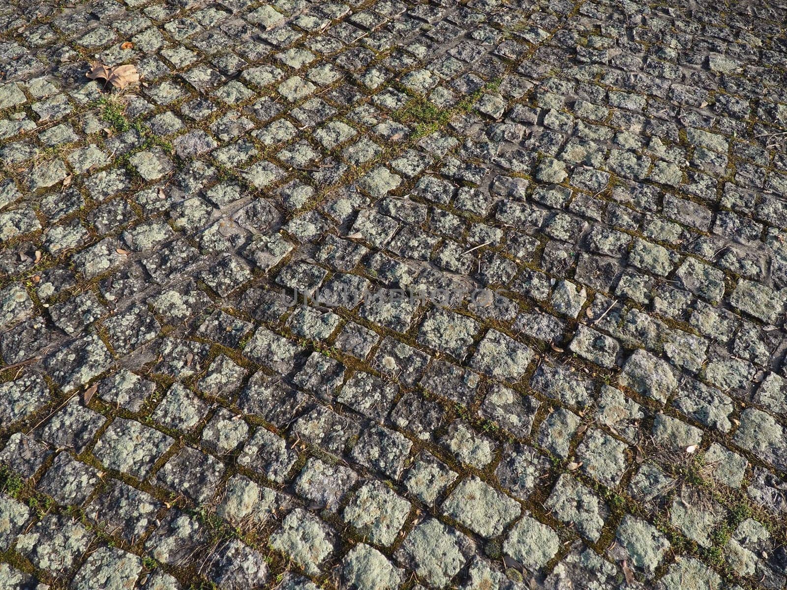 Neatly laid out old paving stones. Pavement on the square of the old town. Square and rectangular stones on the ground, covered with moss and lichens.