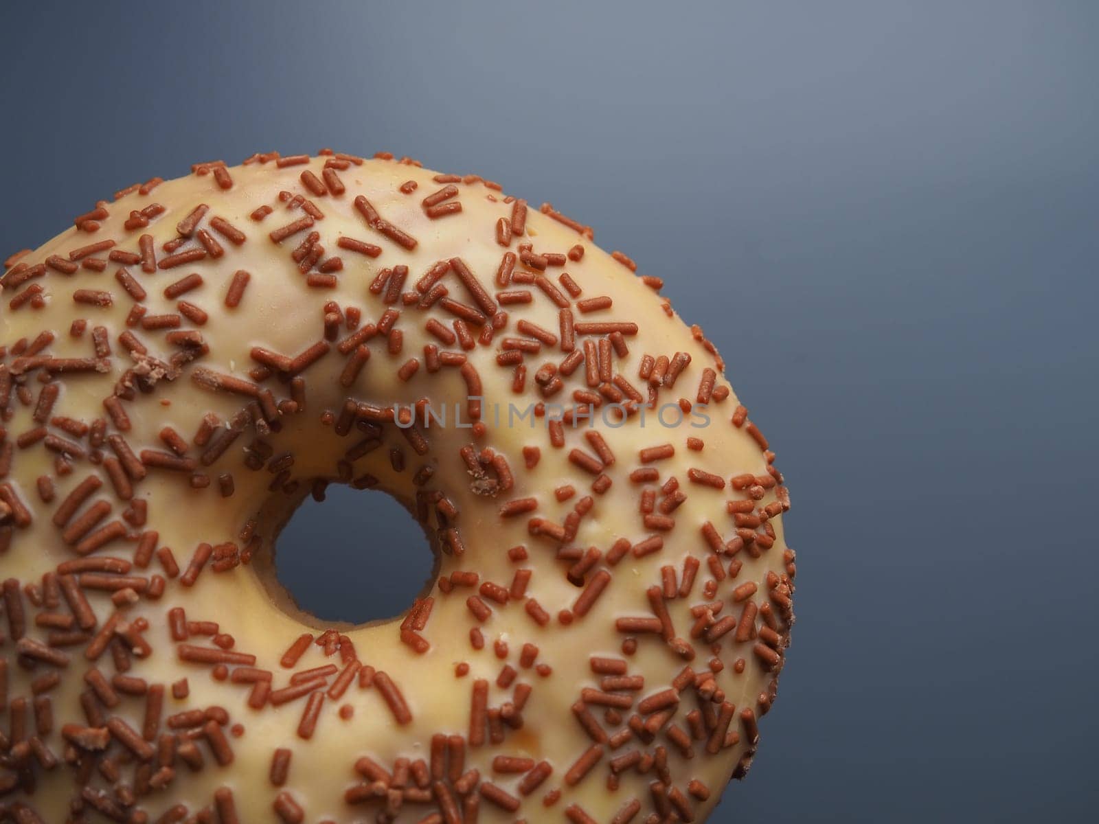 A doughnut or donut. A type of leavened fried dough. Sweet snack that can be homemade or purchased in bakeries, supermarkets, food stalls. Delicious pie with light icing on a dark gray background.