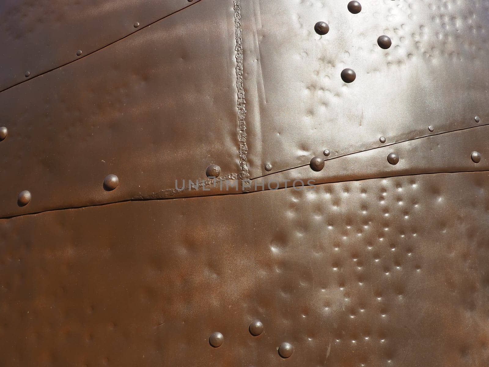 Metal surface with rivets and bolts. Abstract background of a military or industrial nature. Sheathing with dents, seams and nuts. Fasteners on metal. Steel or bronze panel.