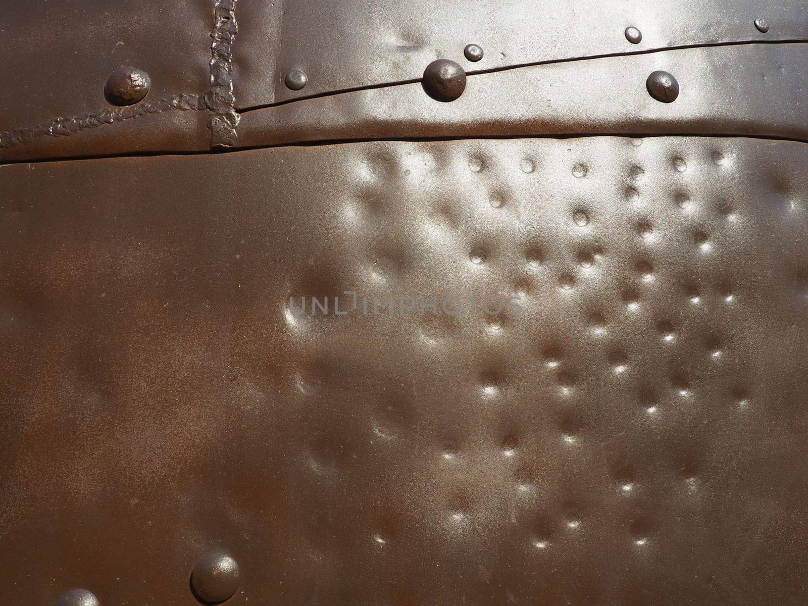 Metal surface with rivets and bolts. Abstract background of a military or industrial nature. Sheathing with dents, seams and nuts. Fasteners on metal. Steel or bronze panel.