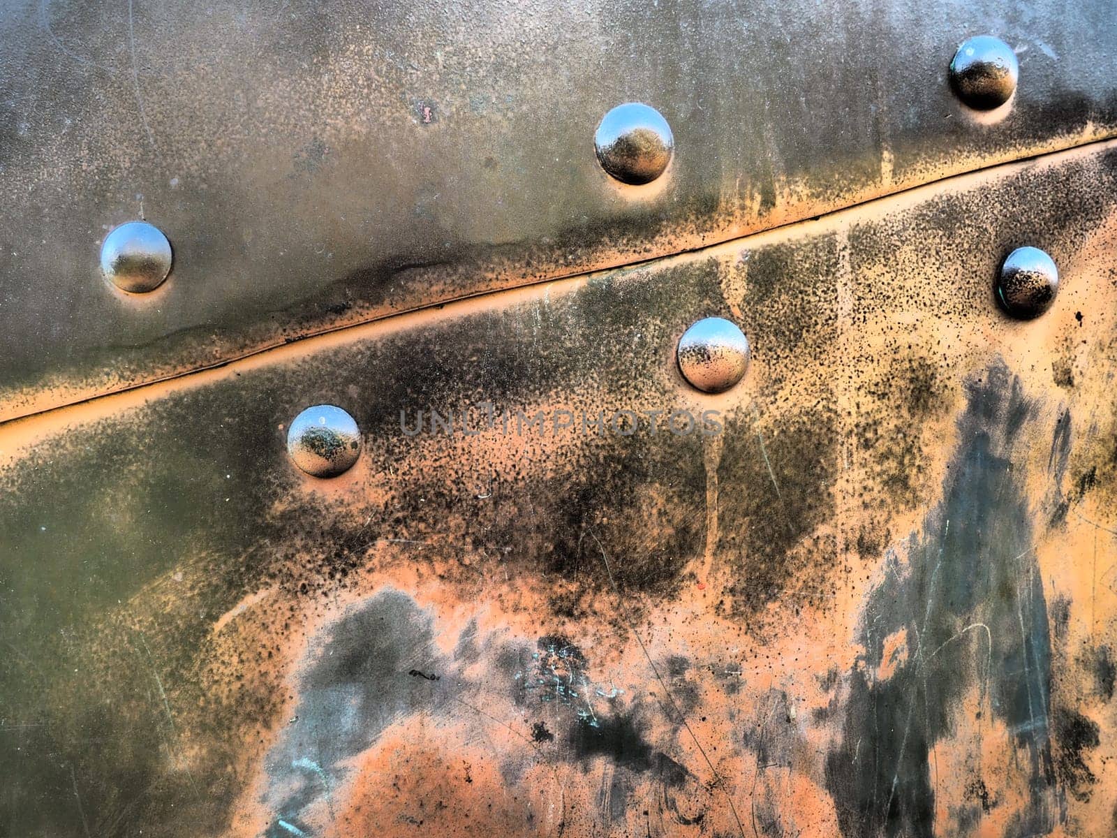 Metal surface with rivets and bolts. Abstract background of a military or industrial nature. Sheathing with dents, seams and nuts. Fasteners on metal. Steel or bronze panel.